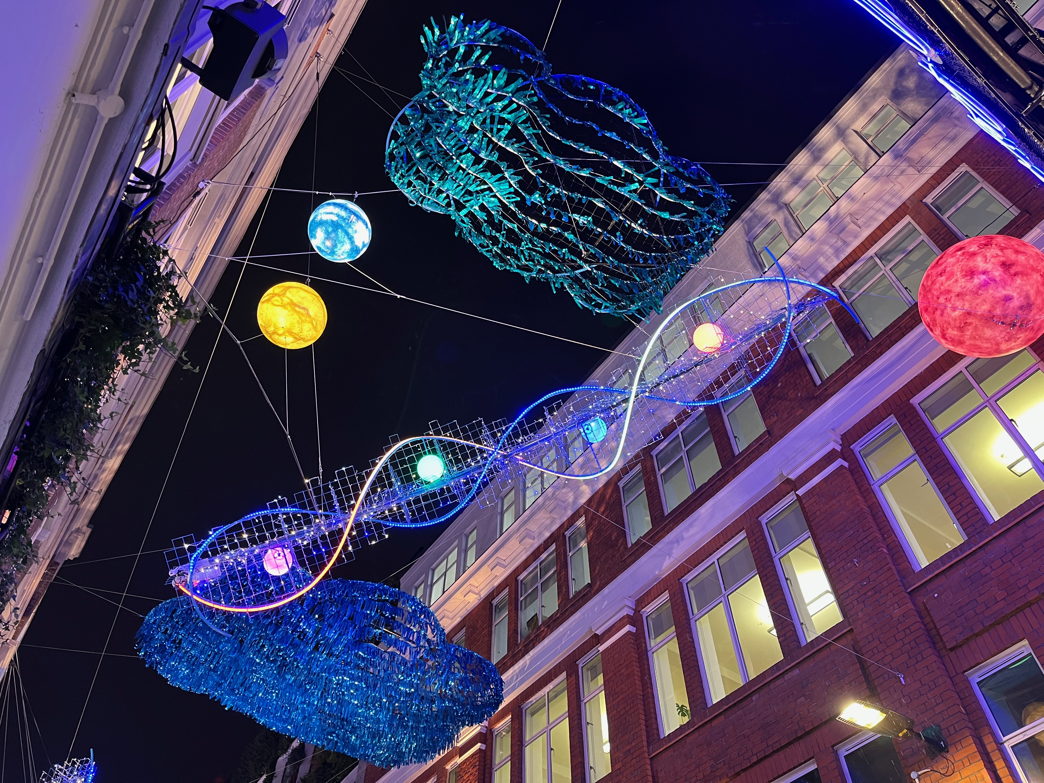 Colourful decorations above Carnaby street, including a couple of small planets and intersecting waves of light.