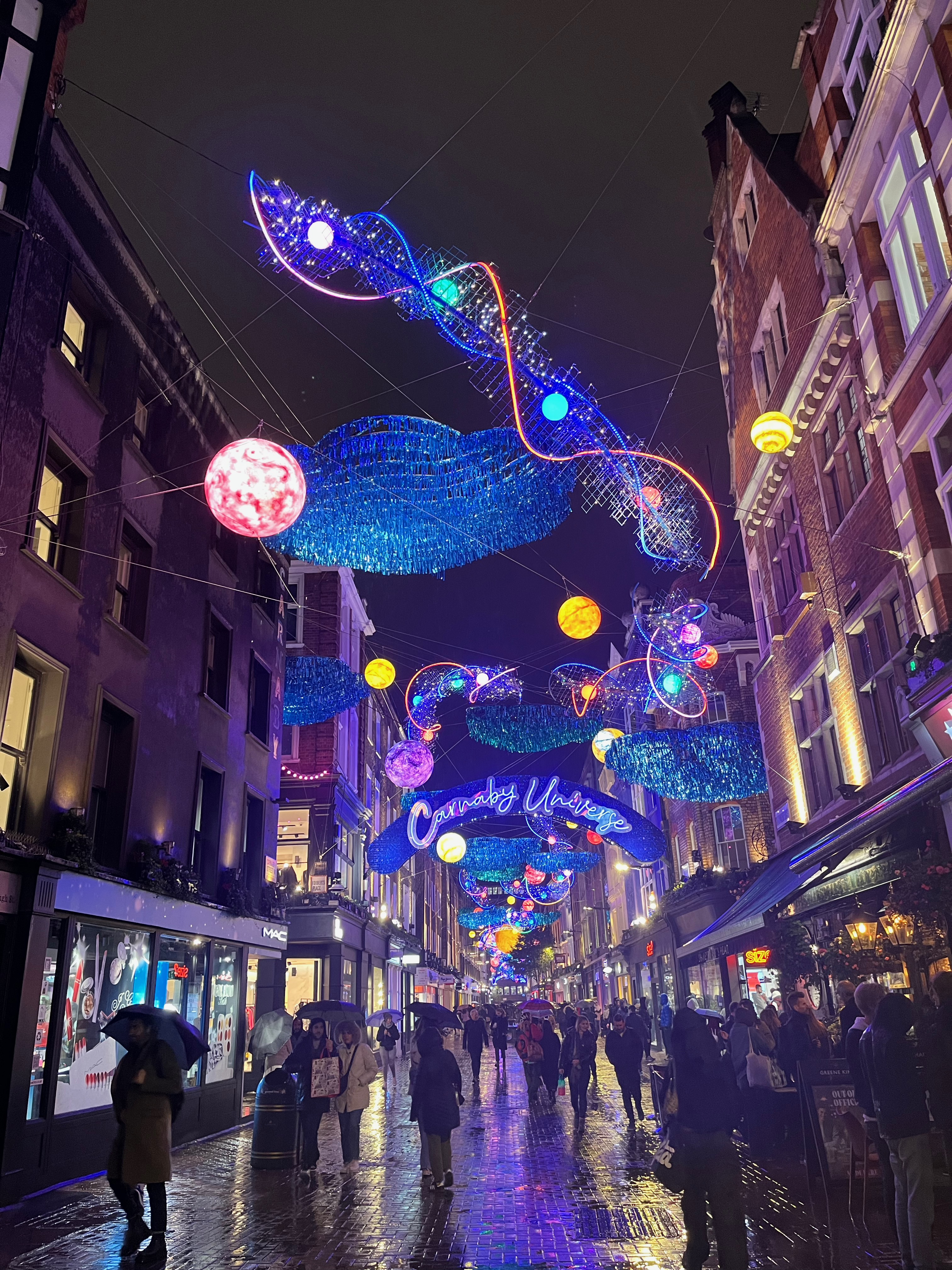 The view from the end of Carnaby Street, with the colourful universe decorations, including planets and waves of light, extending far into the distance.