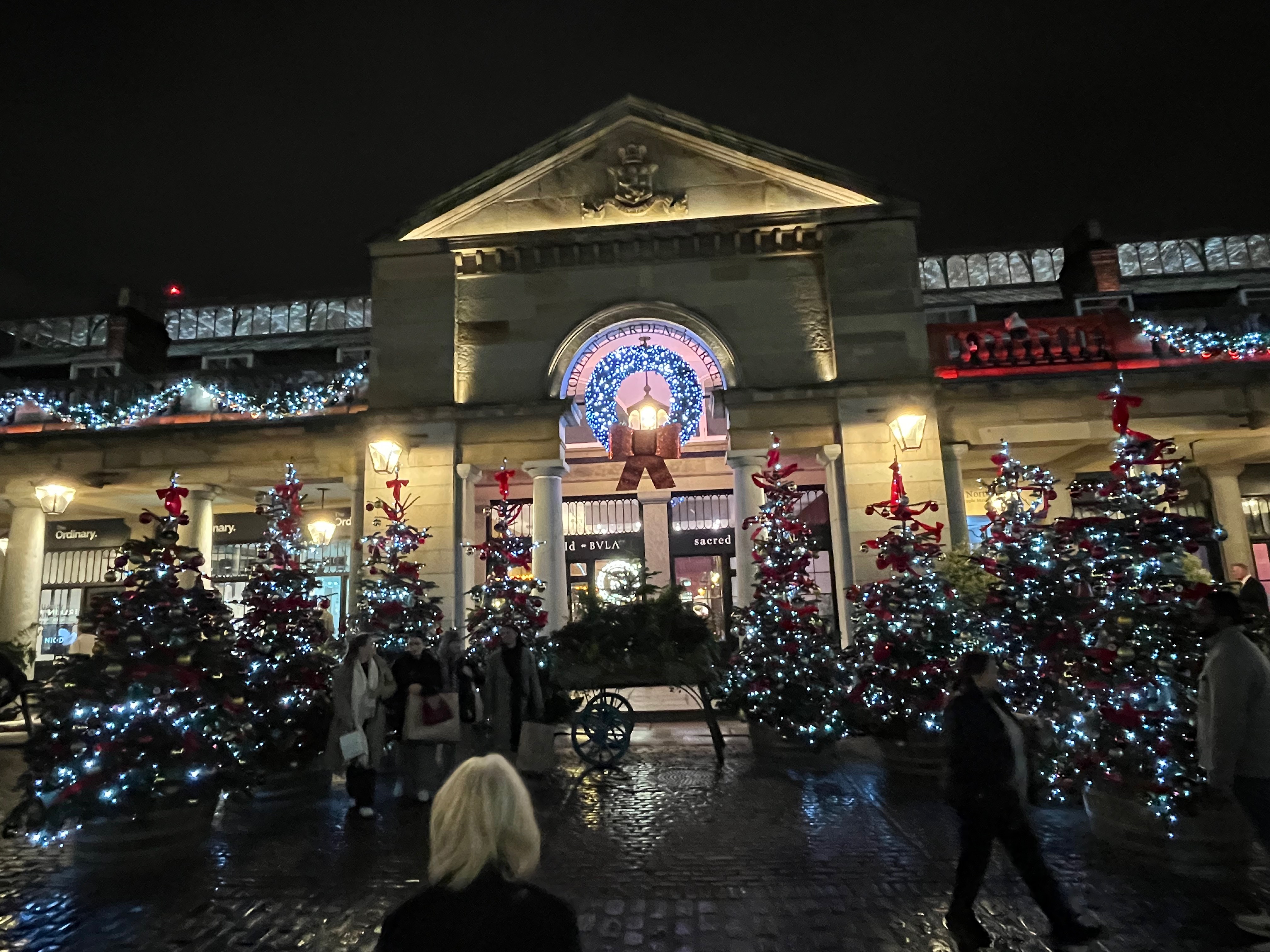 Christmas trees covered in lights, either side of a pathway leading into Covent Garden Market.