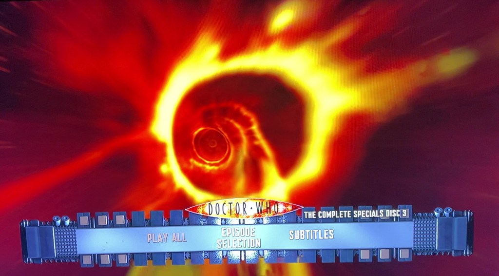 The menu for Disc 3 of the Doctor Who 2008 to 2010 specials Blu-ray steelbook. The screen shows the yellow and red swirling patterns of the time vortex. The menu options are across the bottom of the screen, with the Doctor Who logo just above them.
