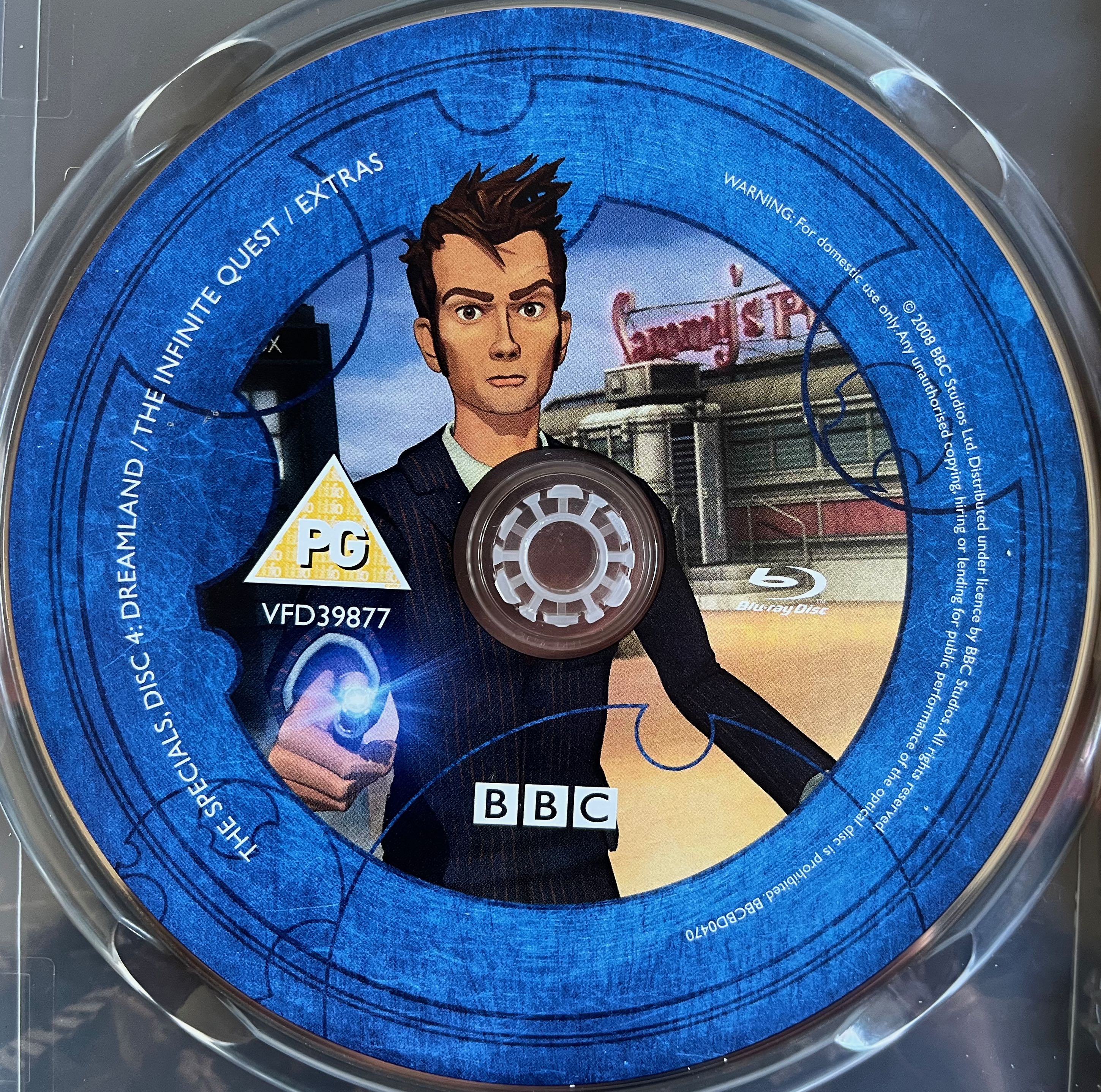 Disc 4 in the Doctor Who 2008 to 2010 Specials Blu-ray set. It features an animated representation of David Tennant's Doctor holding his sonic screwdriver. A blue border around the edge of the disc states that it contains the animated specials Infinite Quest and Dreamland plus extra features, and provides copyright information.