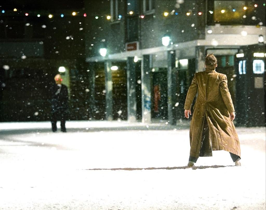 On Rose Tyler's housing estate, David Tennant's Doctor, in his long brown coat, staggers in the snow towards the Tardis, while an Ood watches from a distance.