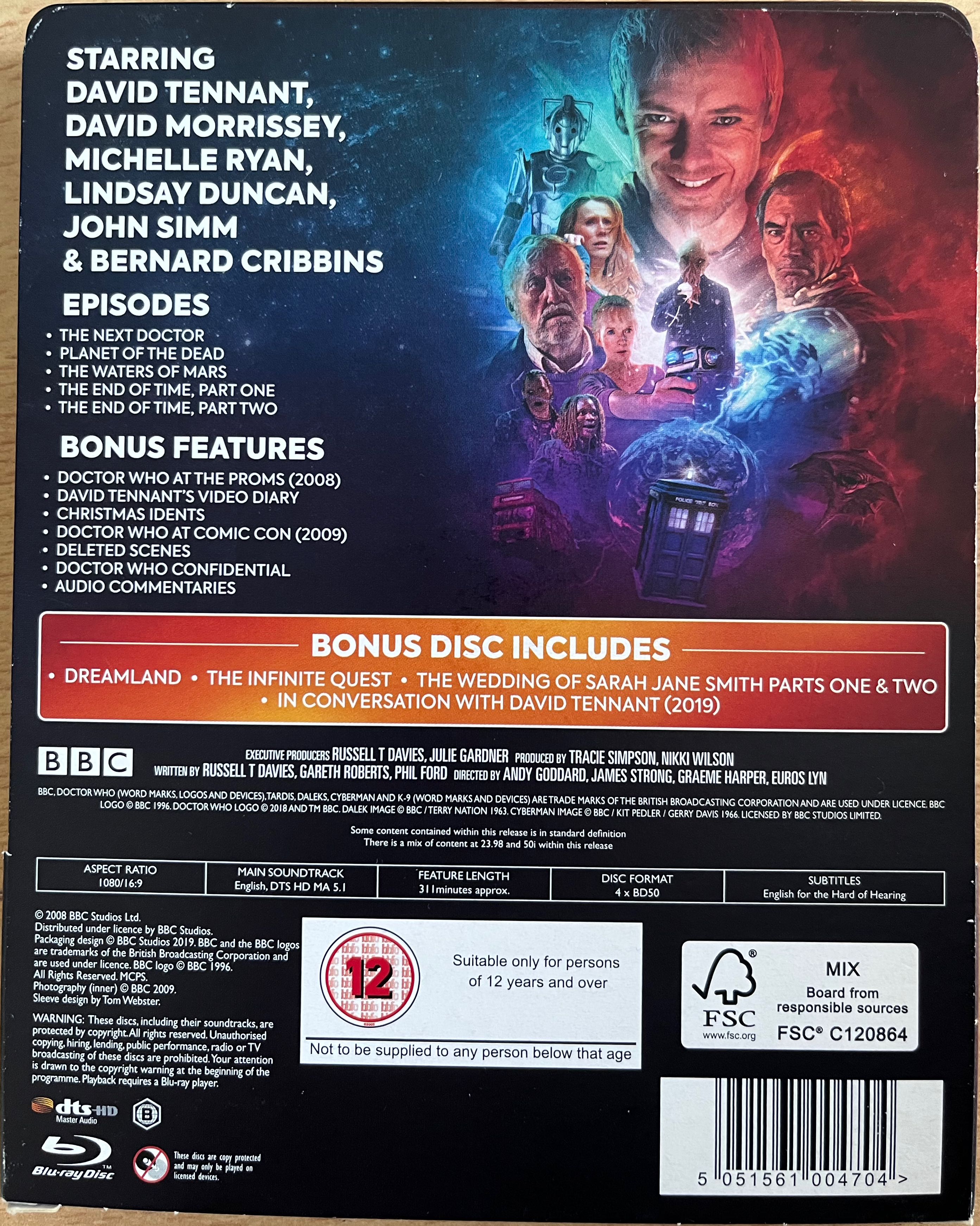 The back cover of the cardboard pocket that houses the Doctor Who 2008 to 2010 Specials Blu-ray Steelbook. A list of the episodes and special features sits alongside artwork of the main enemies and friends that the Doctor encounters during the episodes. There is a large picture of John Simm's grinning face as the Master at the top, with figures below including Donna, her grandfather Wilfred, Timothy Dalton as a Time Lord, and an Ood with spaghetti-like strands hanging from its mouth, while the Tardis is at the very bottom of the image.