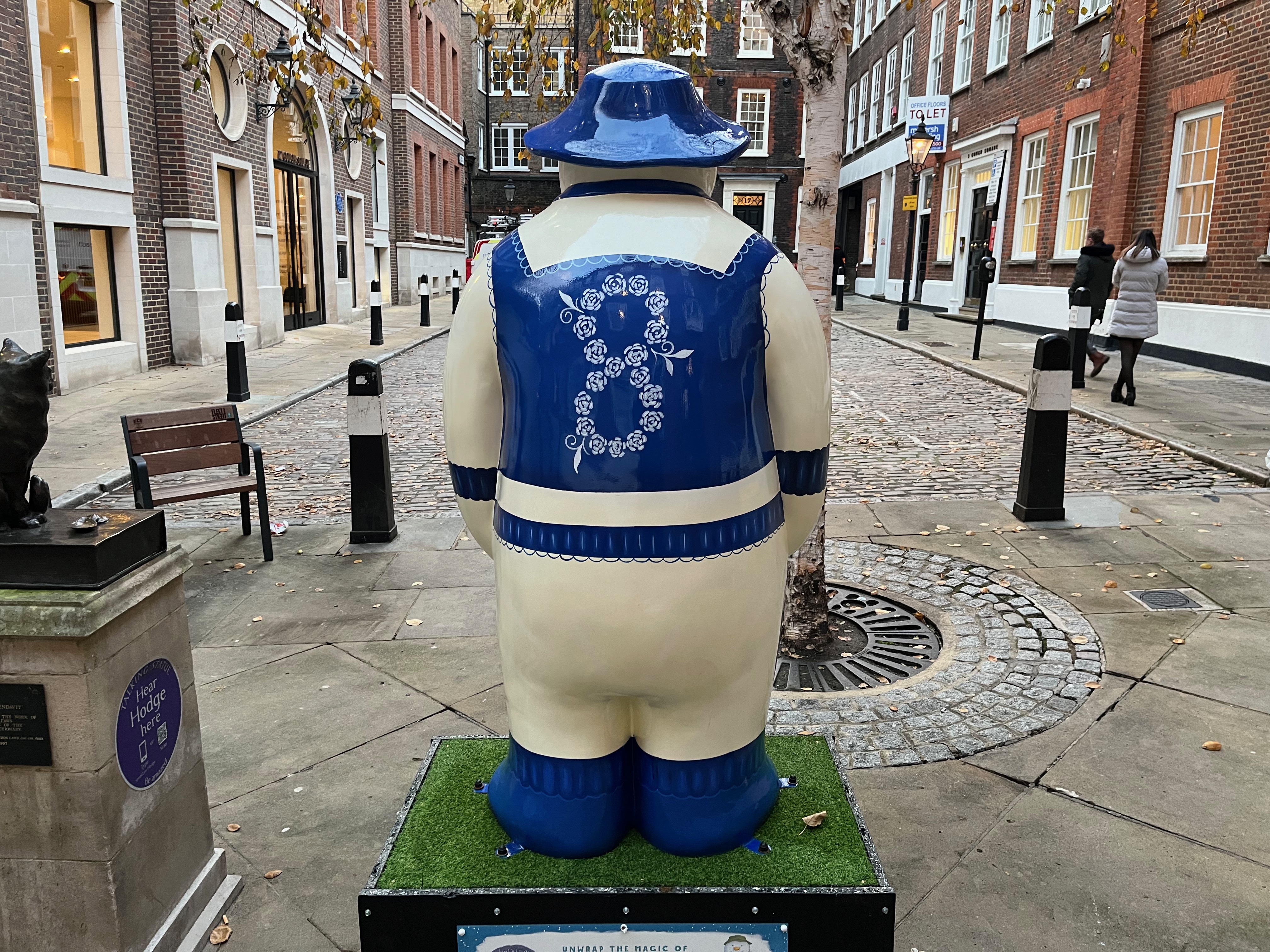 The back of the sculpture of The Snowman called Eight Maids a-Milking, wearing a maid's apron, shoes and a hat that are all dark blue in colour. The back of the apron has a large figure eight made out of white flowers.