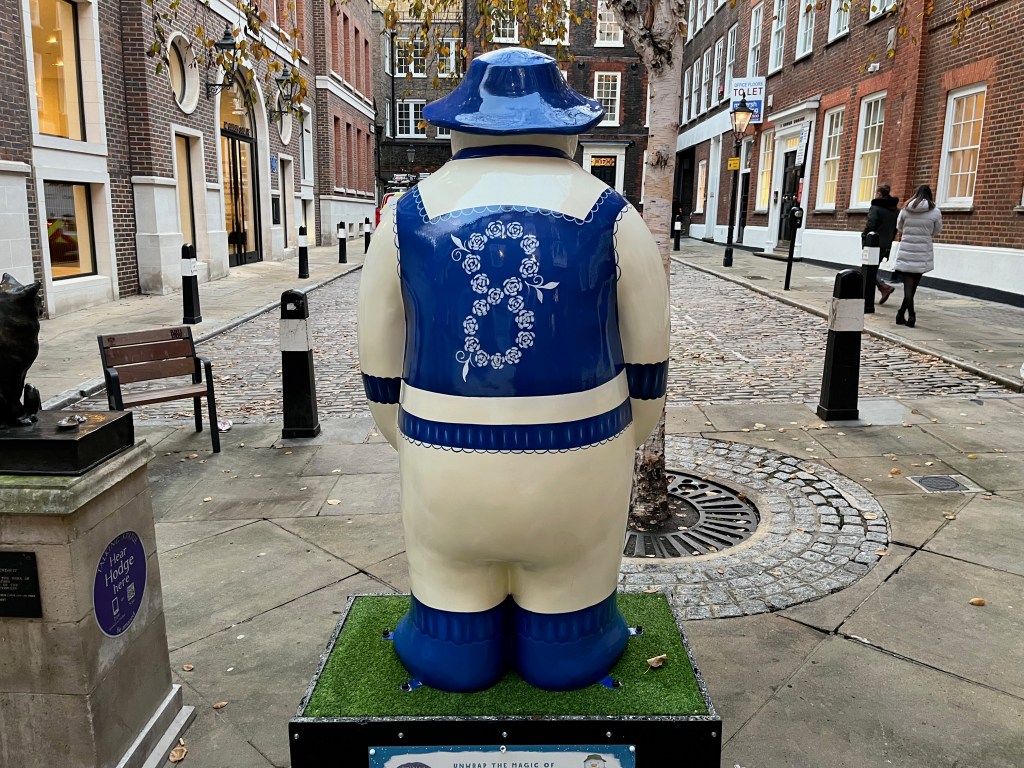 The back of the sculpture of The Snowman called Eight Maids a-Milking, wearing a maid's apron, shoes and a hat that are all dark blue in colour. The back of the apron has a large figure eight made out of white flowers.