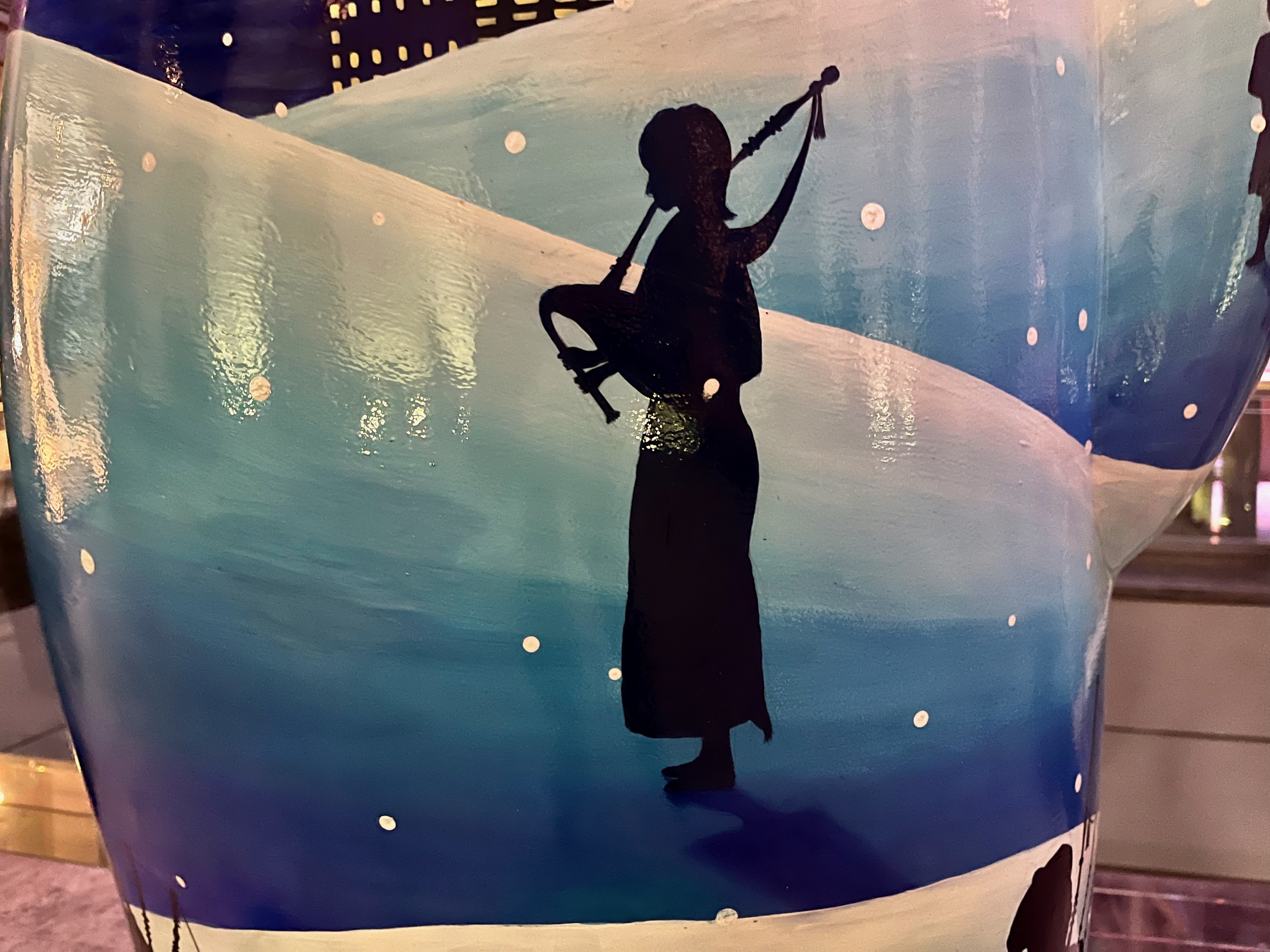 The silhouette of a bagpiper standing on a snowy hillside, on the Snowman sculpture called Eleven Pipers Piping.