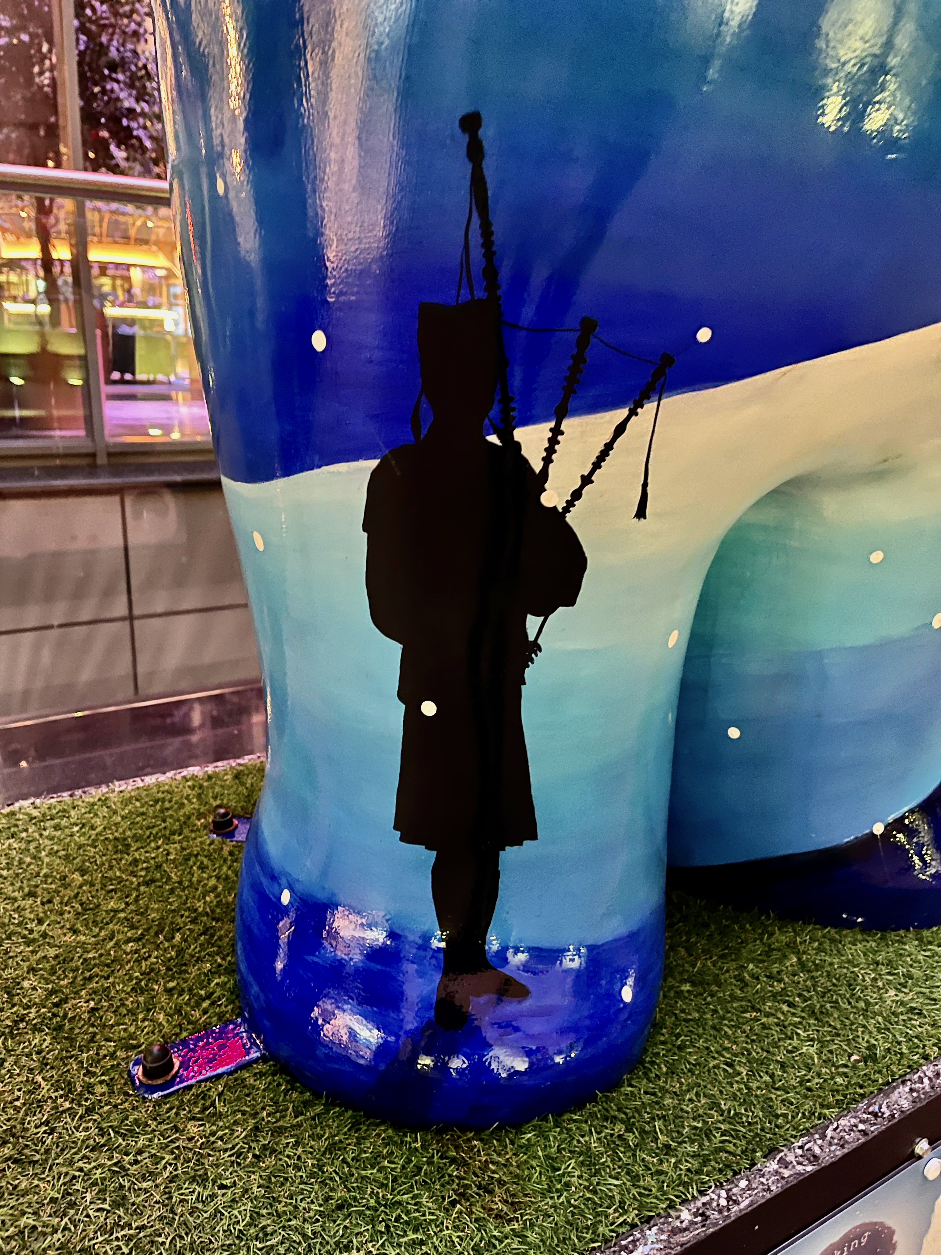 The silhouette of a bagpiper standing on a snowy hill in front of a dark blue night sky, on the Snowman sculpture called Eleven Pipers Piping.