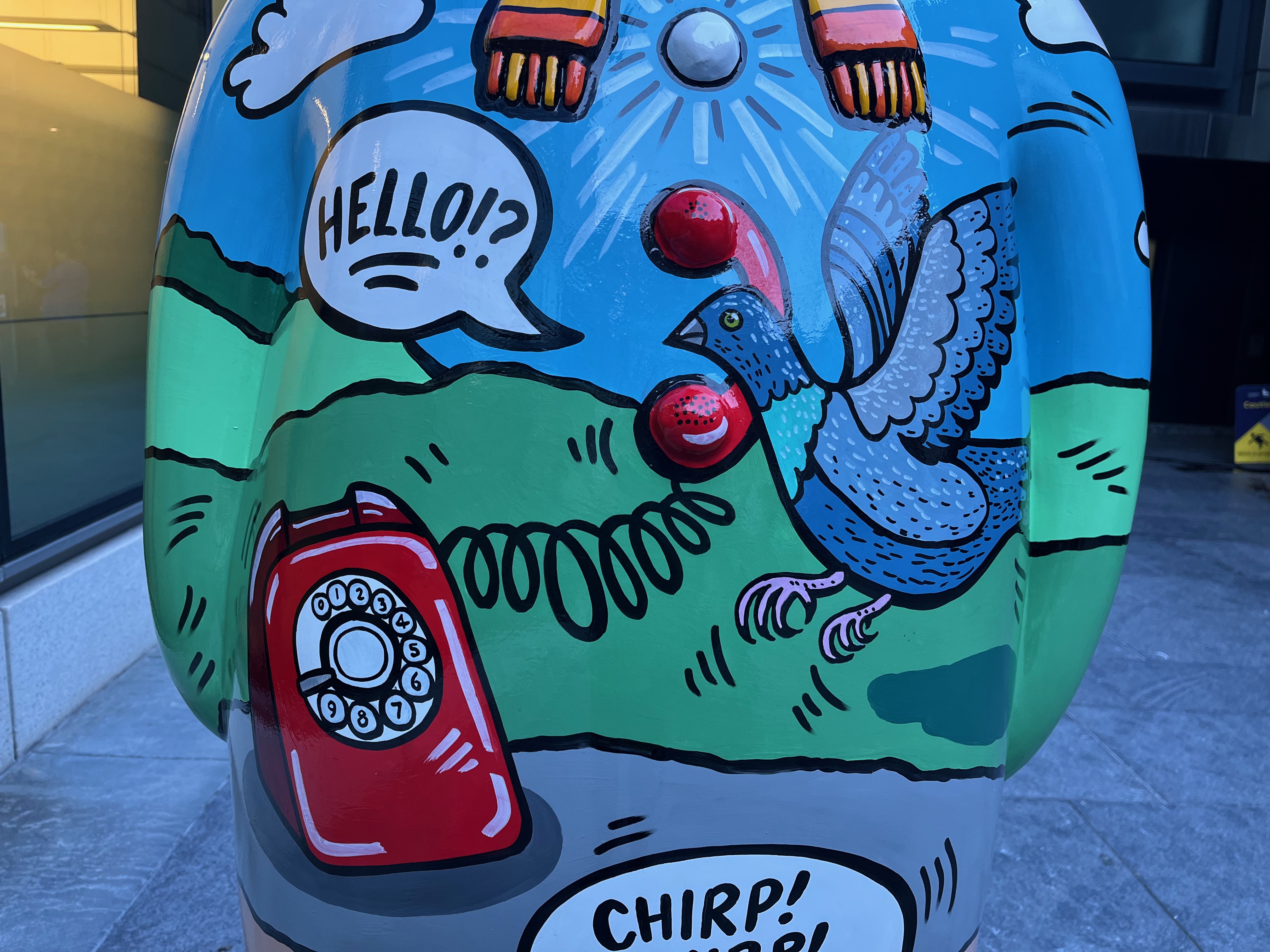 Close-up of a sculpture of The Snowman called Four Calling Birds, showing a blue-coloured bird hovering next to the receiver of a red rotary dial phone, with a speech bubble coming out of it that says Hello?