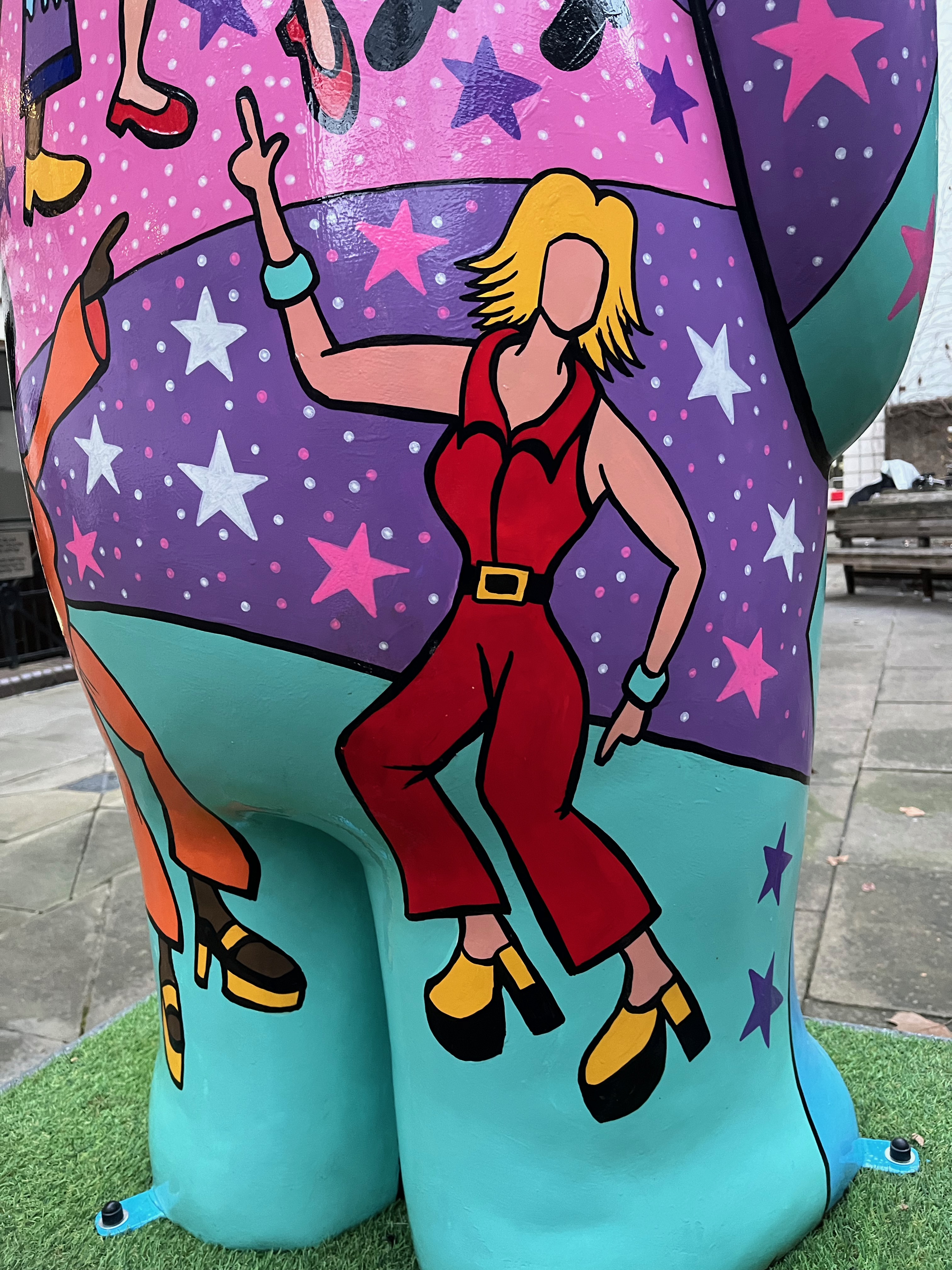 Close-up of a disco diva dancing on the side of the Snowman sculpture called Nine Ladies Dancing. She's a white lady with blonde hair wearing a sleeveless red jumpsuit.