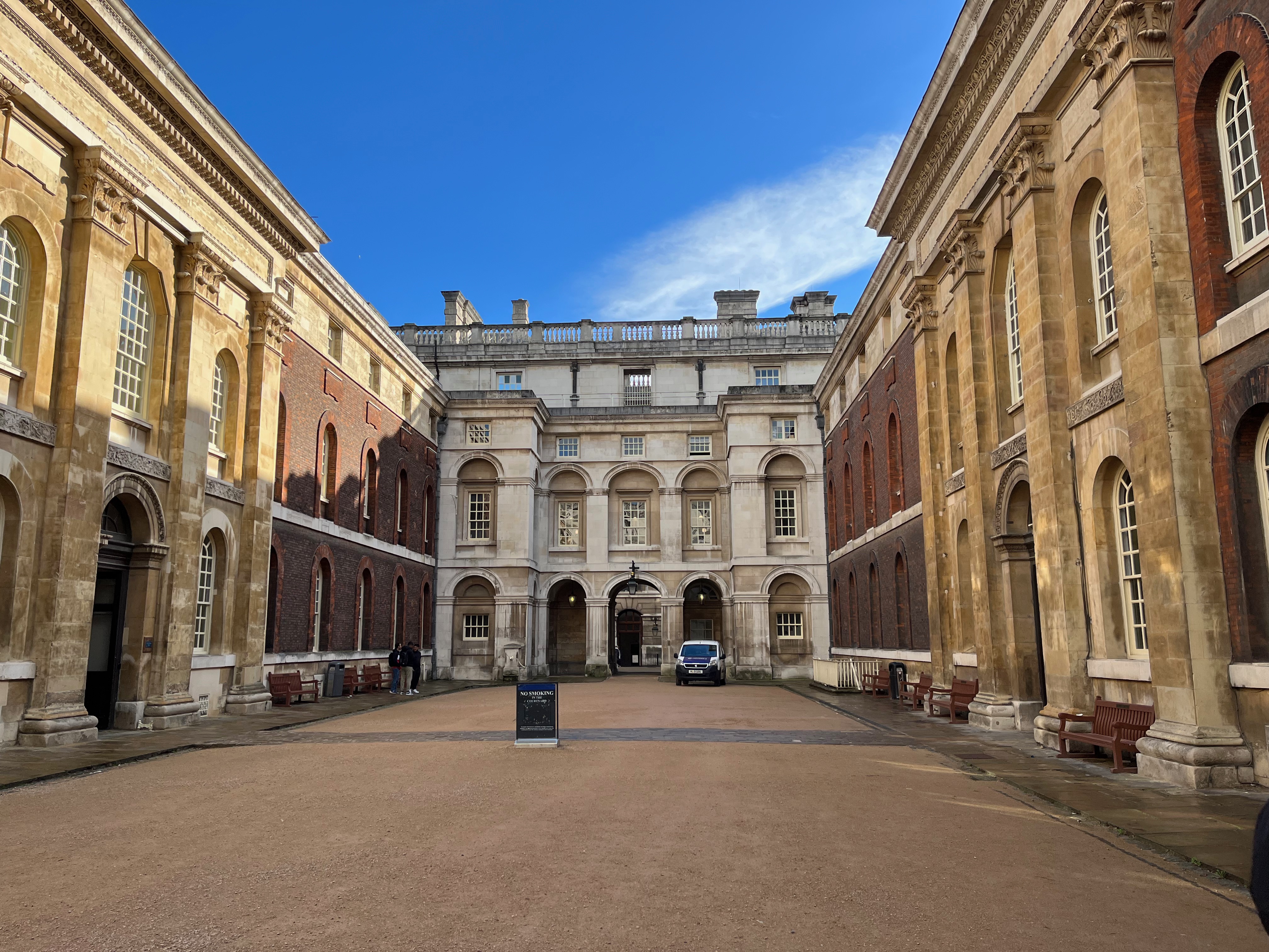 A fairly small, enclosed courtyard at the Old Royal Naval college, with buildings 3 stories high made of white stone or red brickwork.