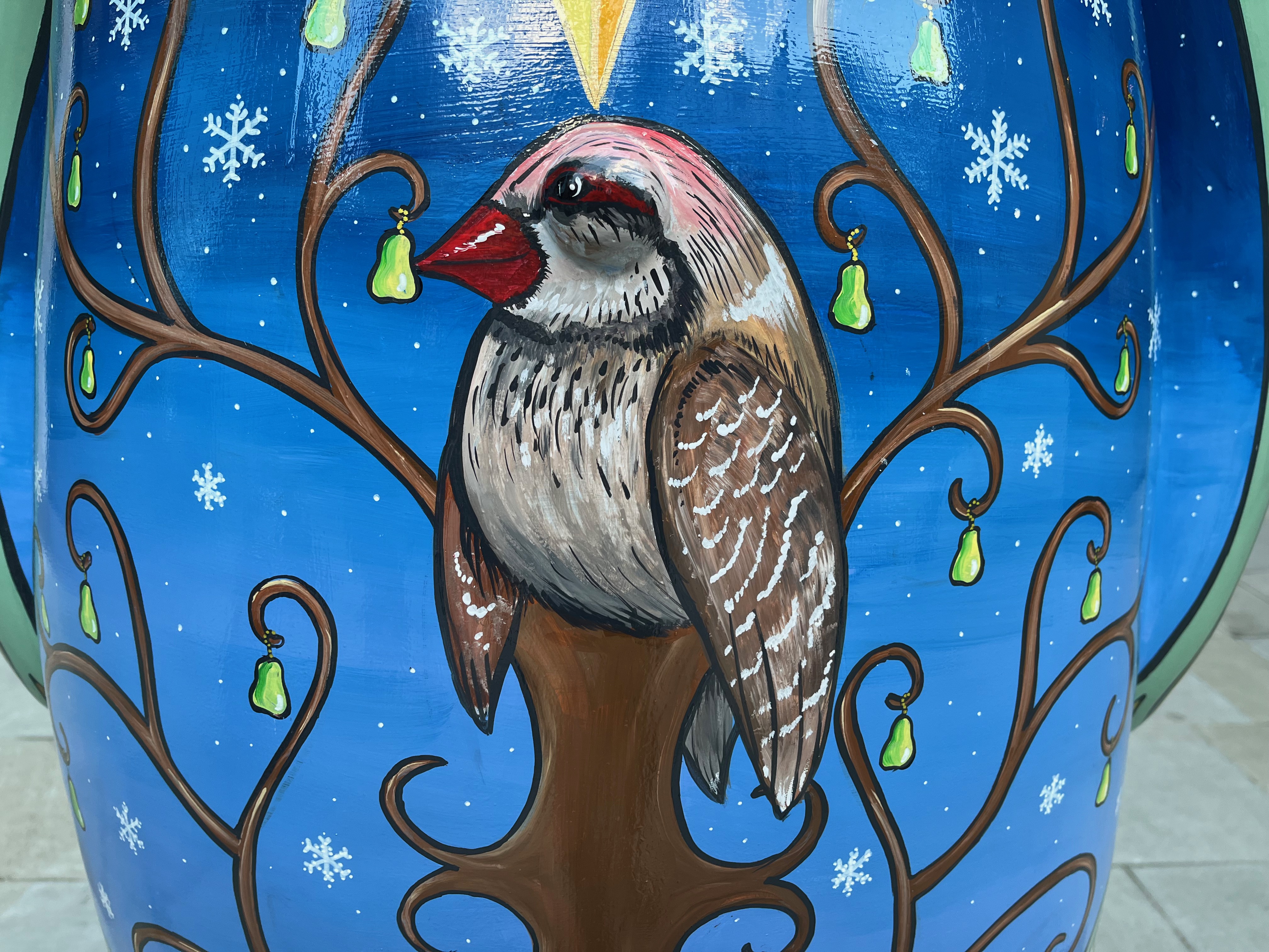 Closeup of the painting of a partridge sitting in a pear tree on the Snowman statue.