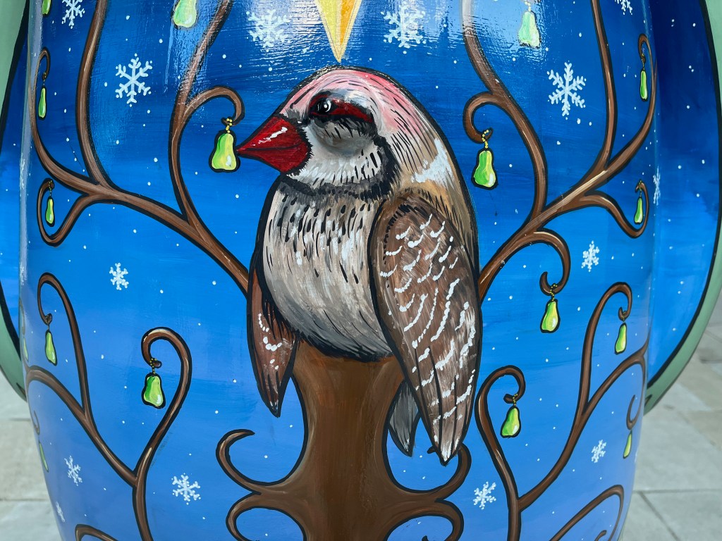Closeup of the painting of a partridge sitting in a pear tree on the Snowman statue.