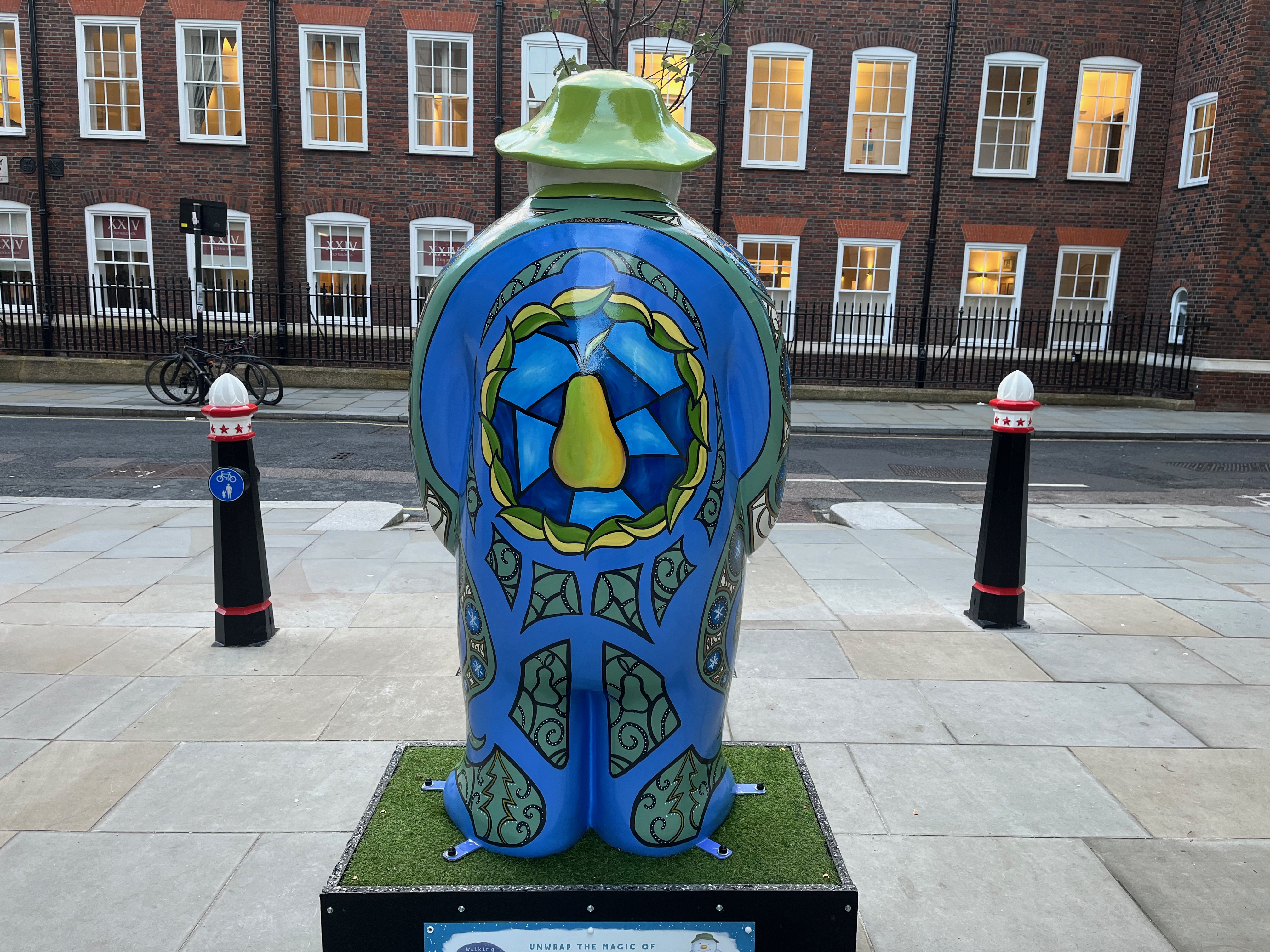 The back of The Snowman statue called Partridge In A Pear Tree, showing a big green pear surrounded by a large wreath made of green leaves. The rest of the Snowman's back is mainly blue in colour, but there are some green segments that contain patterns or little drawings of pears in black.