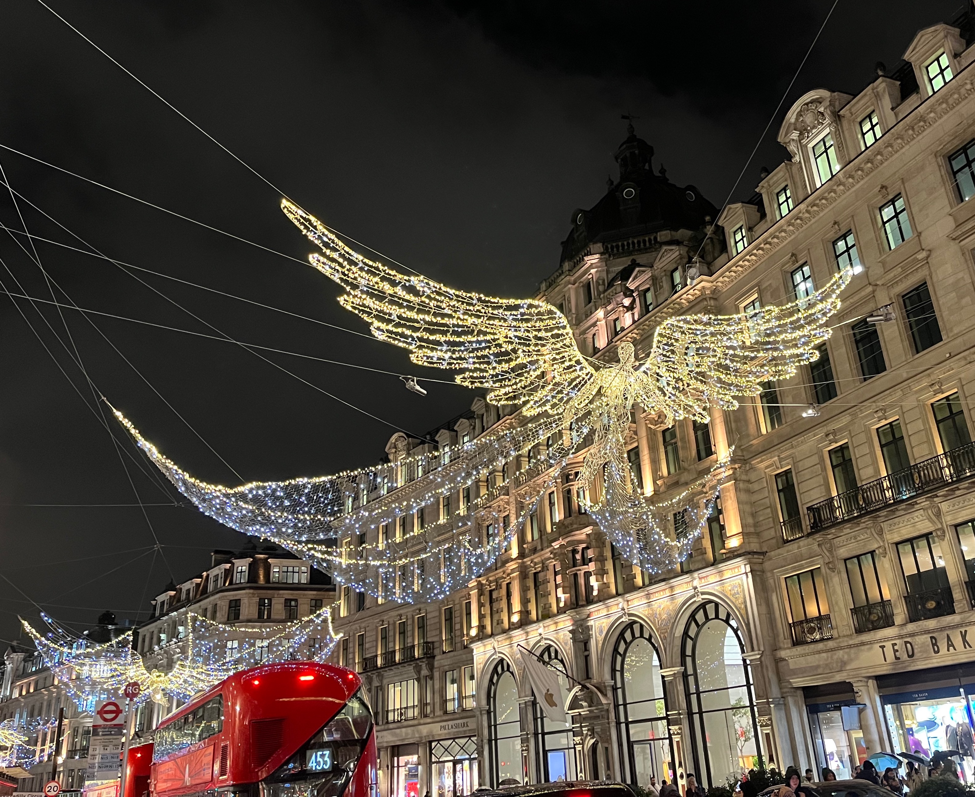 A lit-up figure of an angel with large wings stretched out to the sides, and three huge tail wings fanned out behind them, hanging over Regent Street.