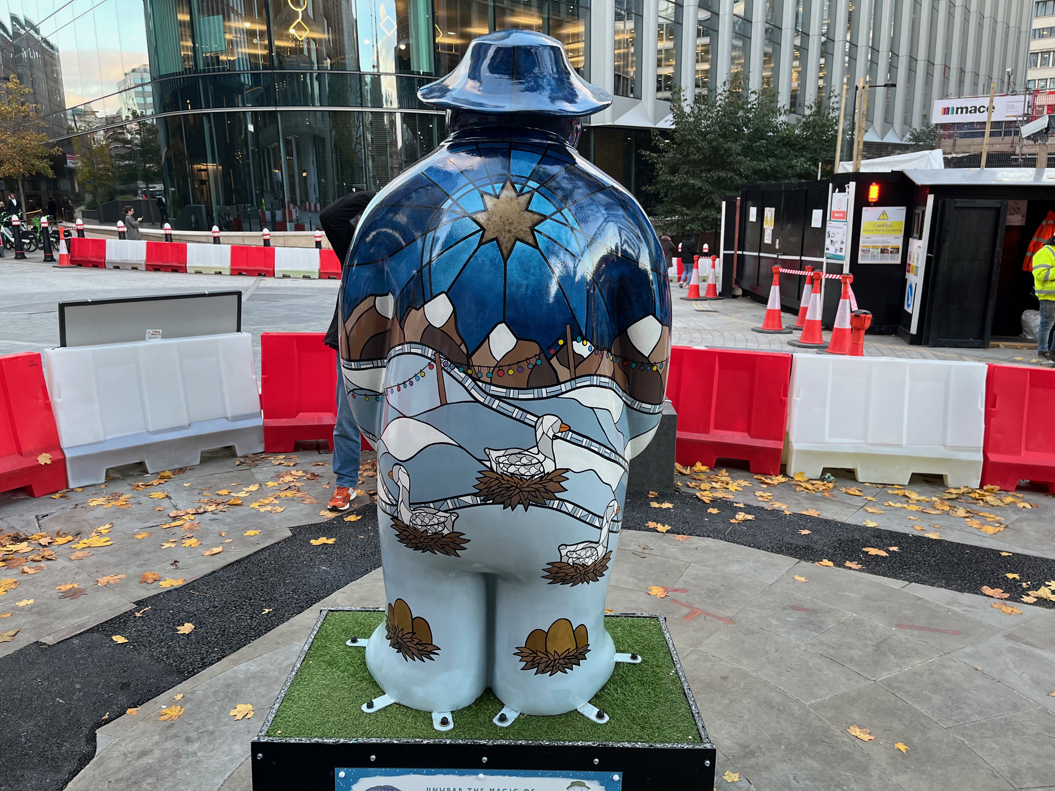 Back of the sculpture of The Snowman called Six Geese a-Laying. His back is painted in a style a bit like stained glass, with geese sitting on nests in front of a snowy landscape with snow-topped mountains in the background, beneath a golden star in the sky. Each of his feet also has a nest containing a few eggs.