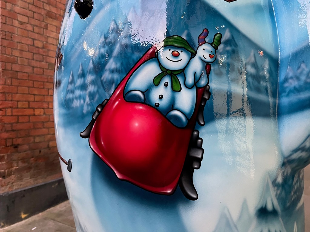 Close-up of the Ten Lords a-Leaping sculpture of the Snowman, showing the character riding in a big red sleigh, with the Snowdog on his shoulder.
