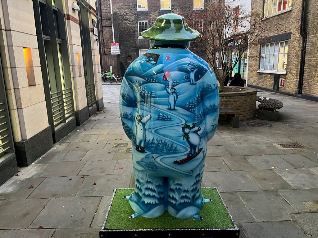 The back of the sculpture of The Snowman called Ten Lords a-Leaping. HIs body is covered in a snowy landscape scene, on which there are lots of images of the Snowman engaging in various activities, including juggling snowballs, skiing, skating, hang-gliding and holding balloons.