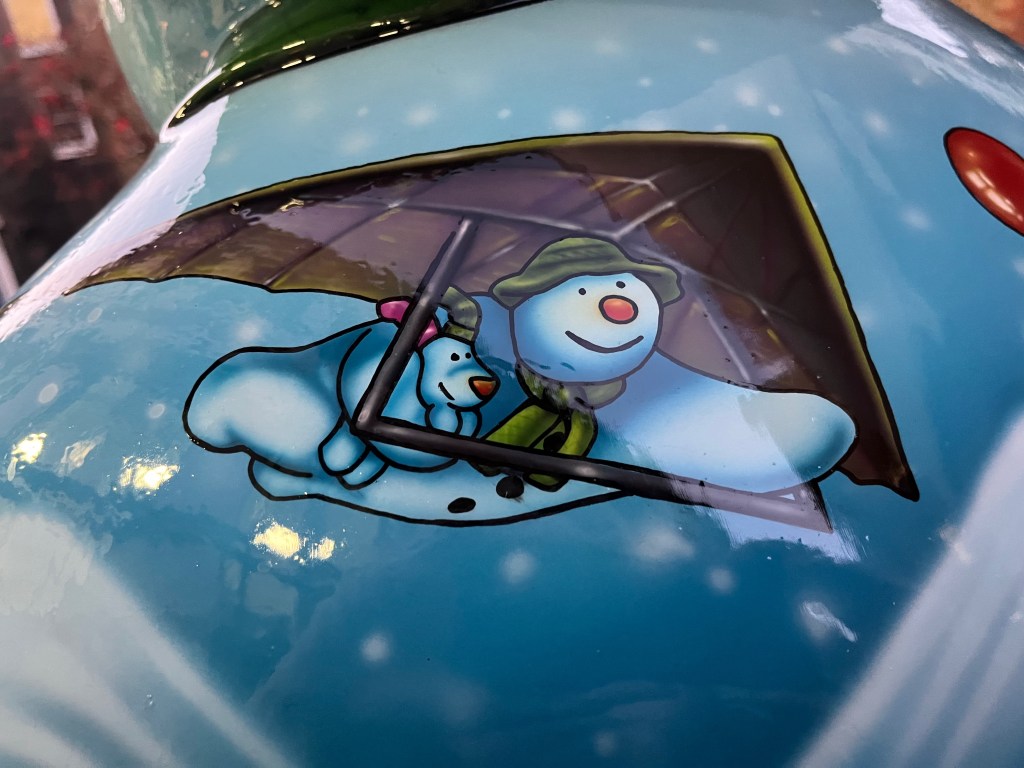 Close-up of the Ten Lords a-Leaping sculpture of the Snowman, showing the character hang-gliding, and carrying the Snowdog under one harm.