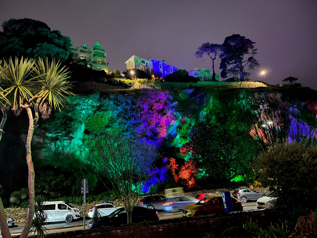 The cliffs of Rock Walk Gardens in Torquay, bathed in multicoloured lighting, including yellow, green, blue and purple.