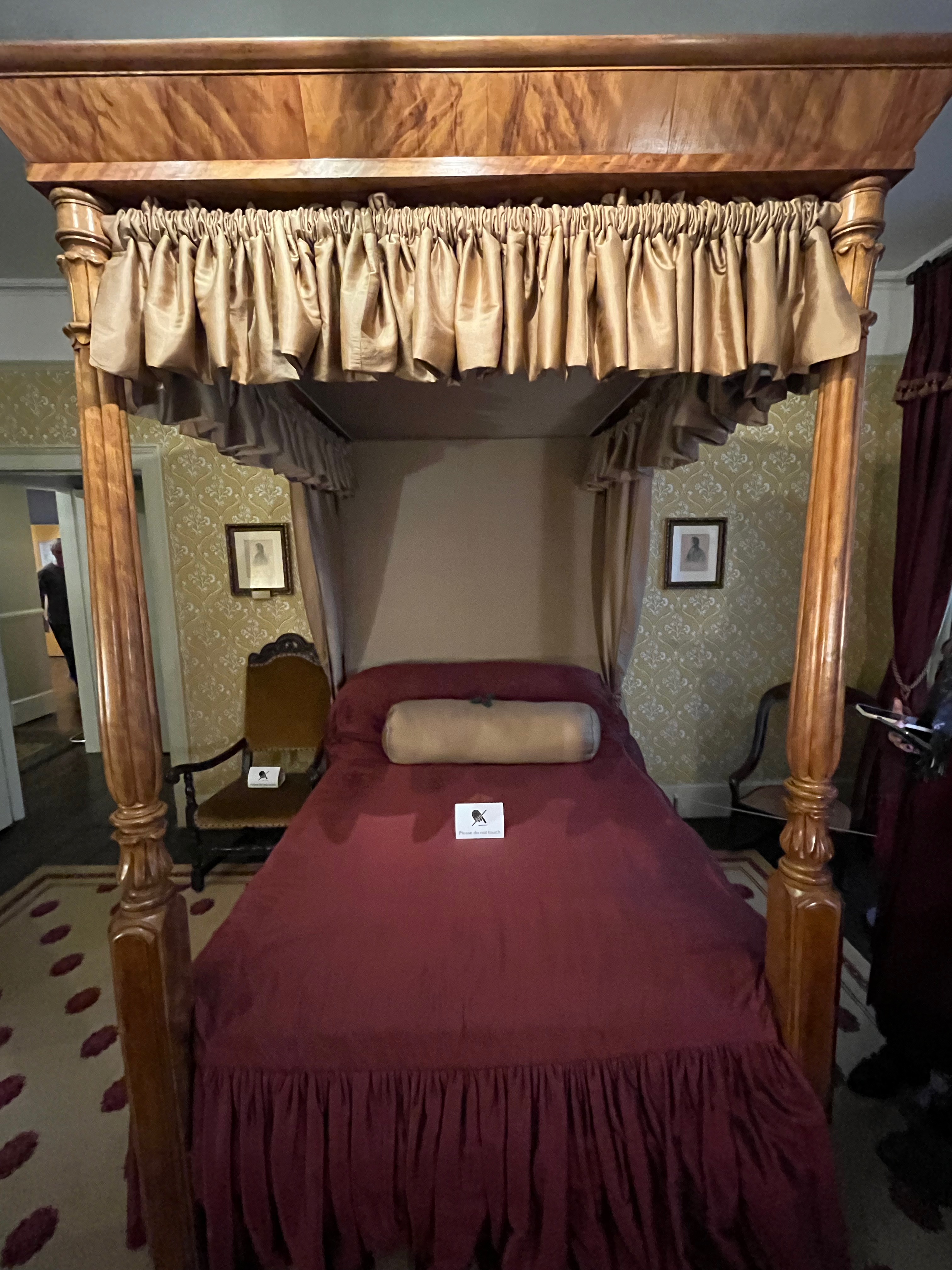 A four poster bed in the Charles Dickens Museum, with red sheets and a long white pillow.