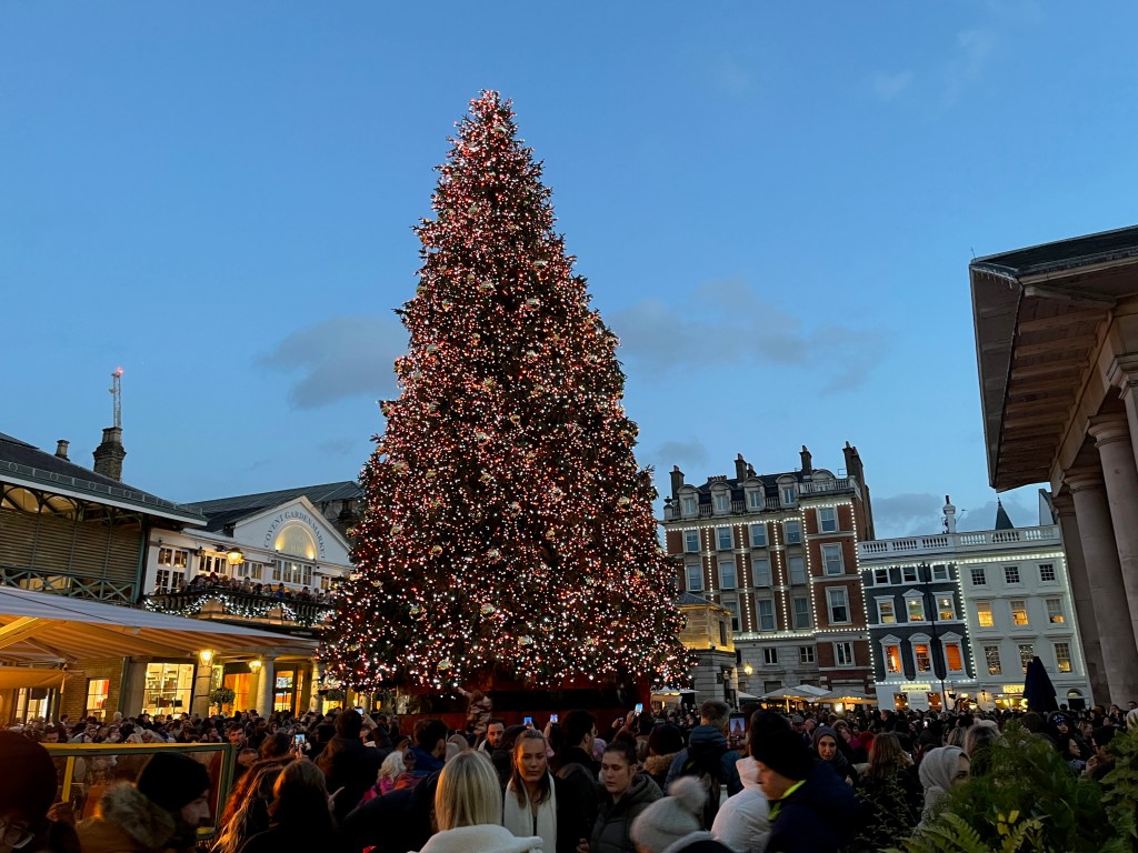 A huge, glittering Christmas tree standing outside, and towering over, the Covent Garden market building.