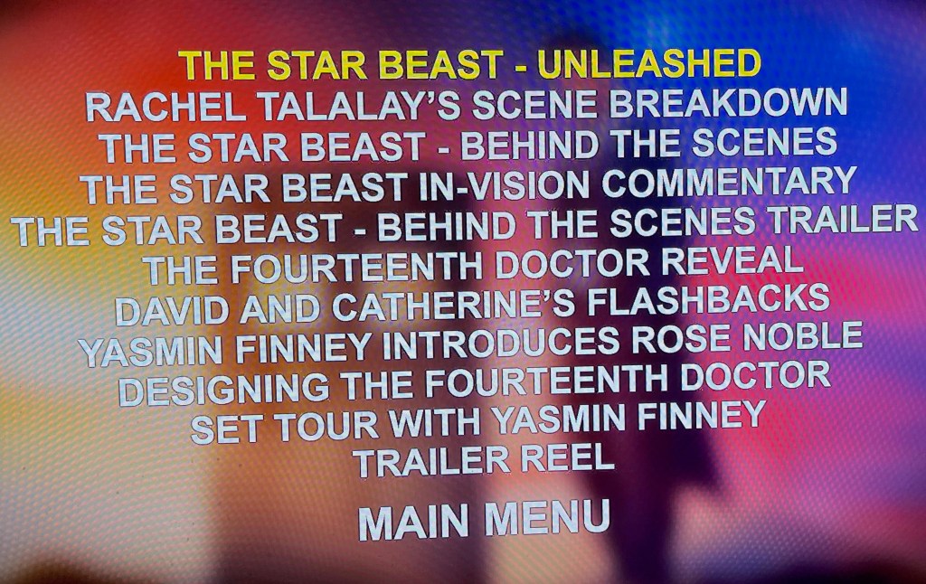 Audio special features menu from the Doctor Who 60th Anniversary Specials Blu-ray. Over a blurred image of the Doctor standing next to the Tardis against a colourful background, large white uppercase text lists all of the bonus material that you can access.