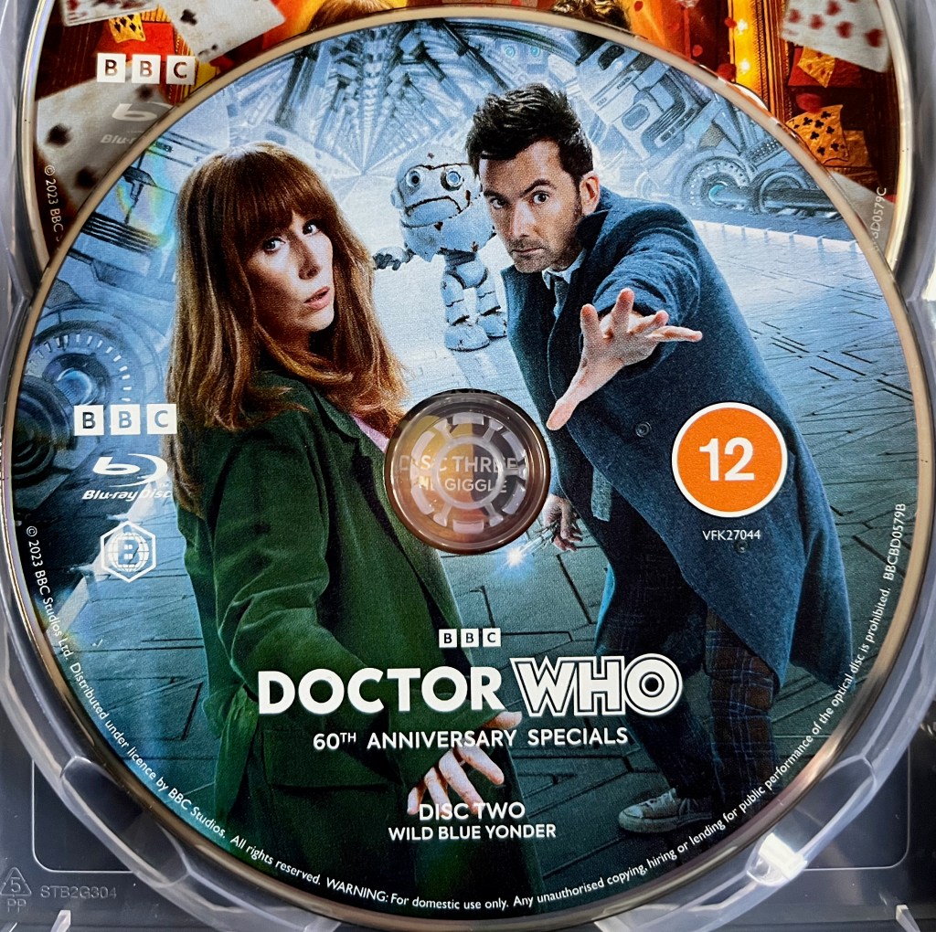 Disc 2 in the Blu-ray steelbook for the Doctor Who 60th Anniversary Specials, containing Wild Blue Yonder. The artwork shows David Tennant's Doctor and Donna Noble standing together in the corridor of a spaceship, looking sideways towards us, the Doctor reaching out his hand towards us. A white robot stands in the background.
