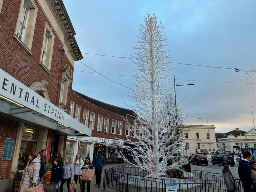 A very tall Christmas tree, covered in white lights, outside Exeter Central railway station.