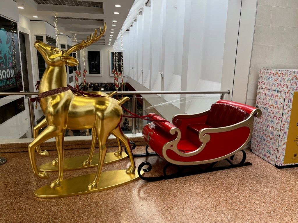 A model of 2 large gold reindeer pulling a red sleigh in Exeter's Guildhall Shopping Centre. Children can fit inside the sleigh to have their photo taken.