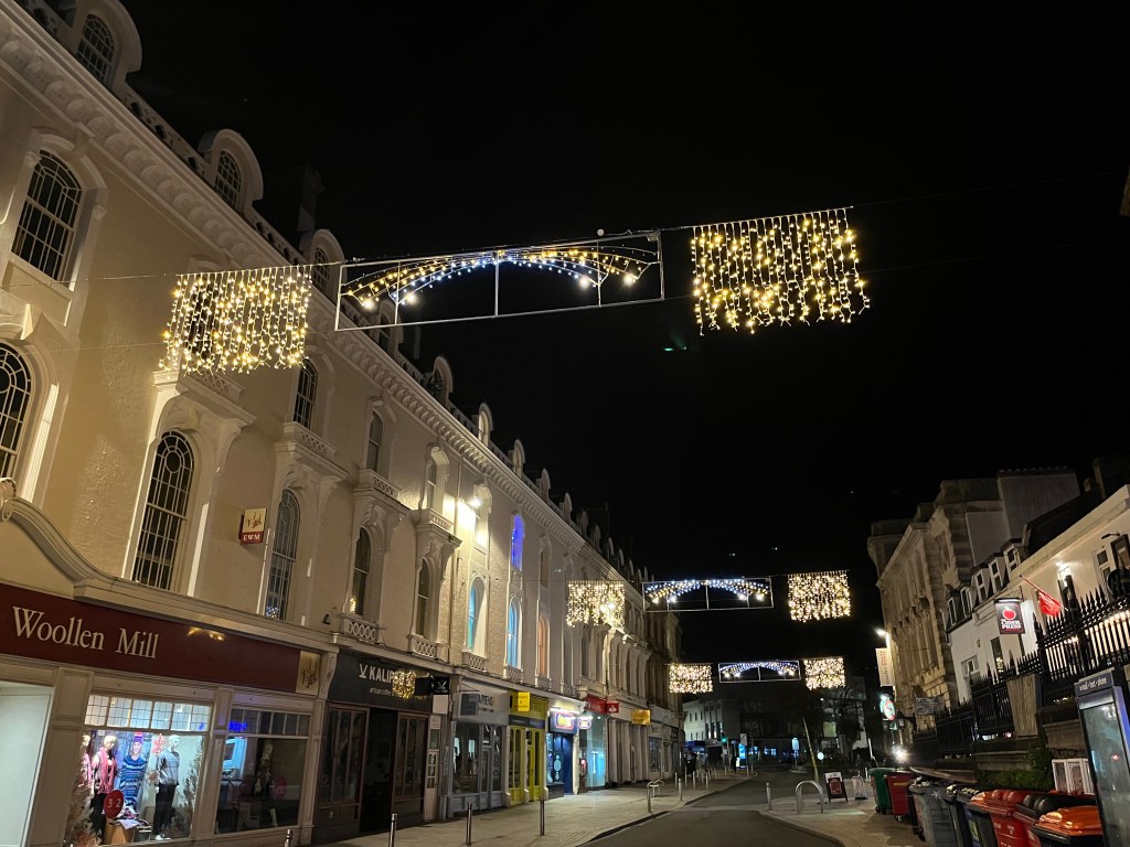 Christmas lights over Fleet Street in Torquay, with brightly lit rectangles either side of a thin, colourful rainbow in the centre.