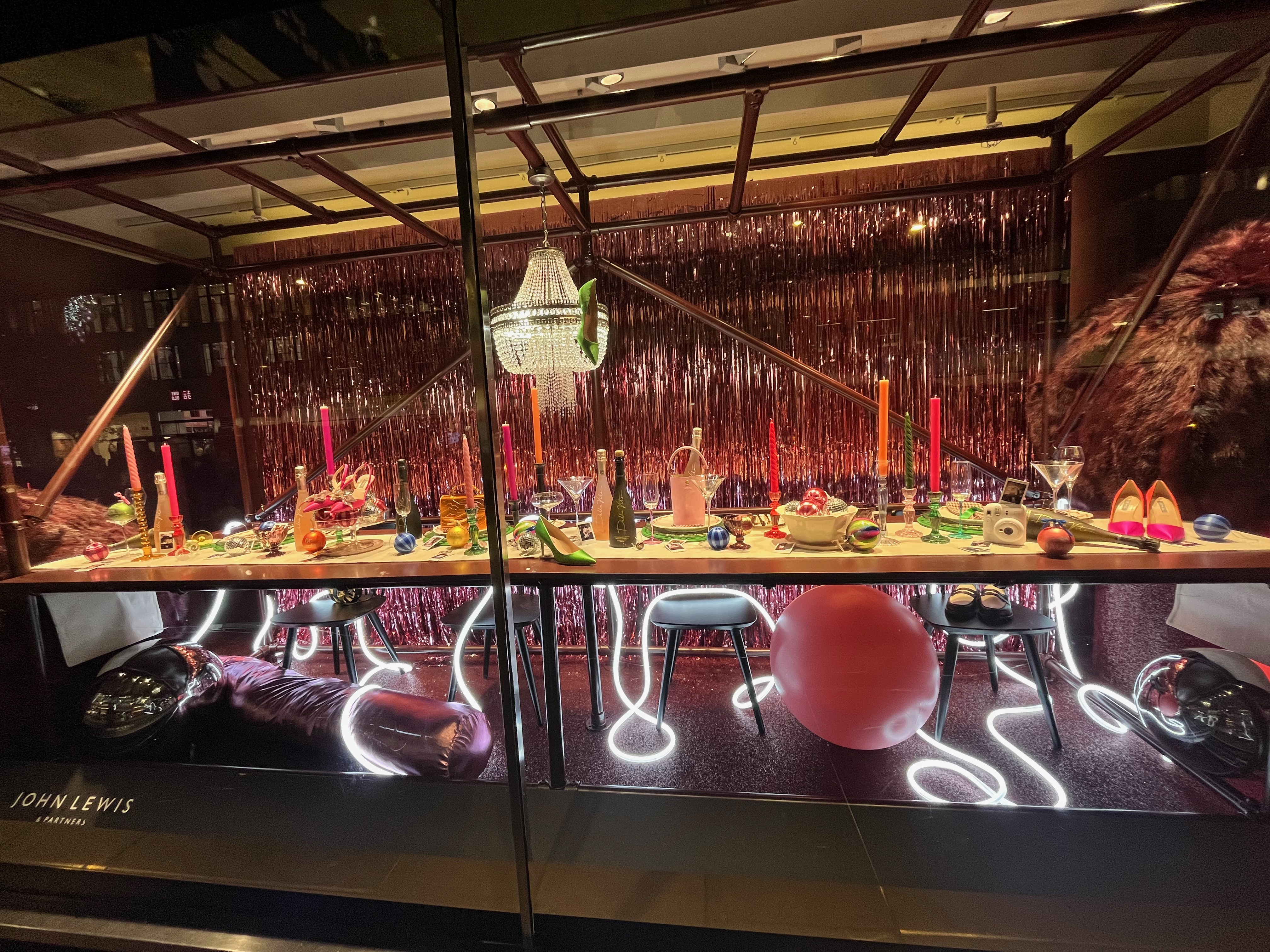 John Lewis Christmas window display, showing a long dining table fully decked out for a festive feast, below an ornate chandelier.