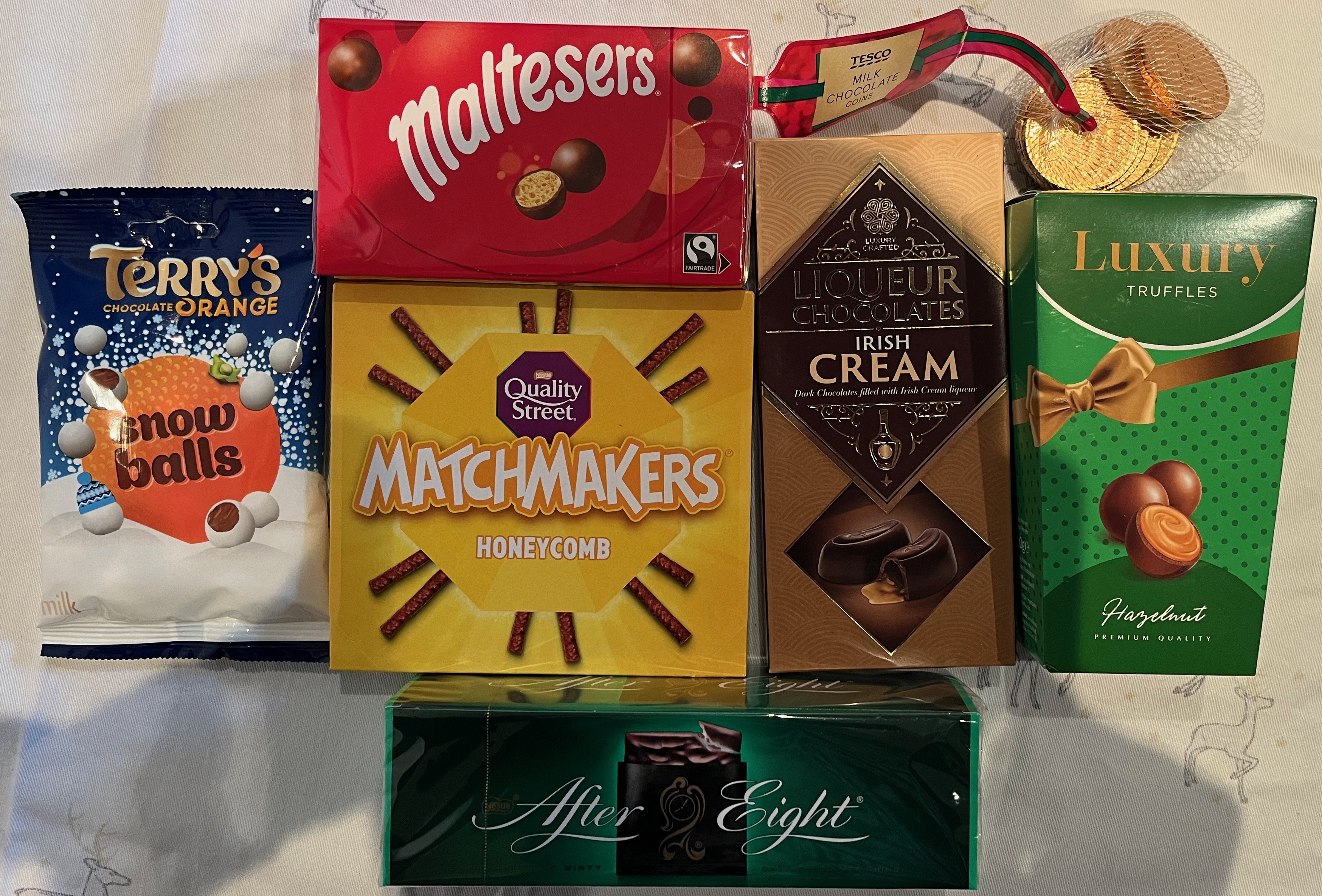 A collection of treats including Terry's Chocolate Orange Snowballs, Maltesers, Quality Street Honeycomb Matchmakers, Tesco Milk Chocolate Coins, Irish Cream Liqueur Chocolates, Luxury Hazelnut Truffles, and After Eight Mints.