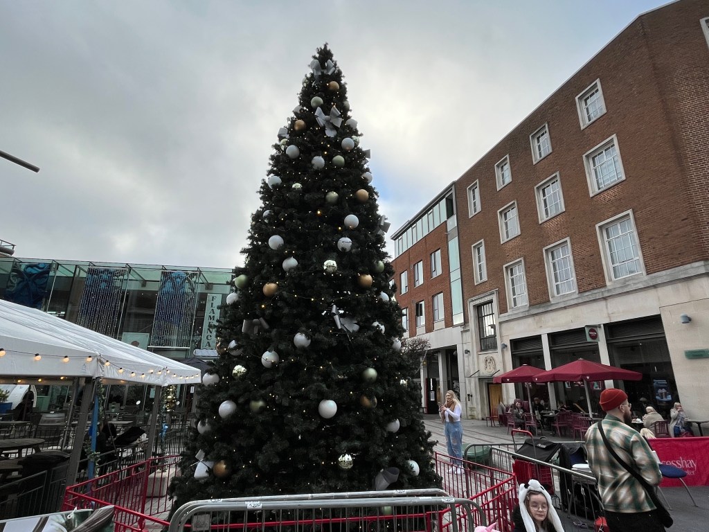 A large Christmas tree covered in white, gold and silver baubles, and lots of small lights, in an outdoor area of the Princesshay shopping centre in Exeter.