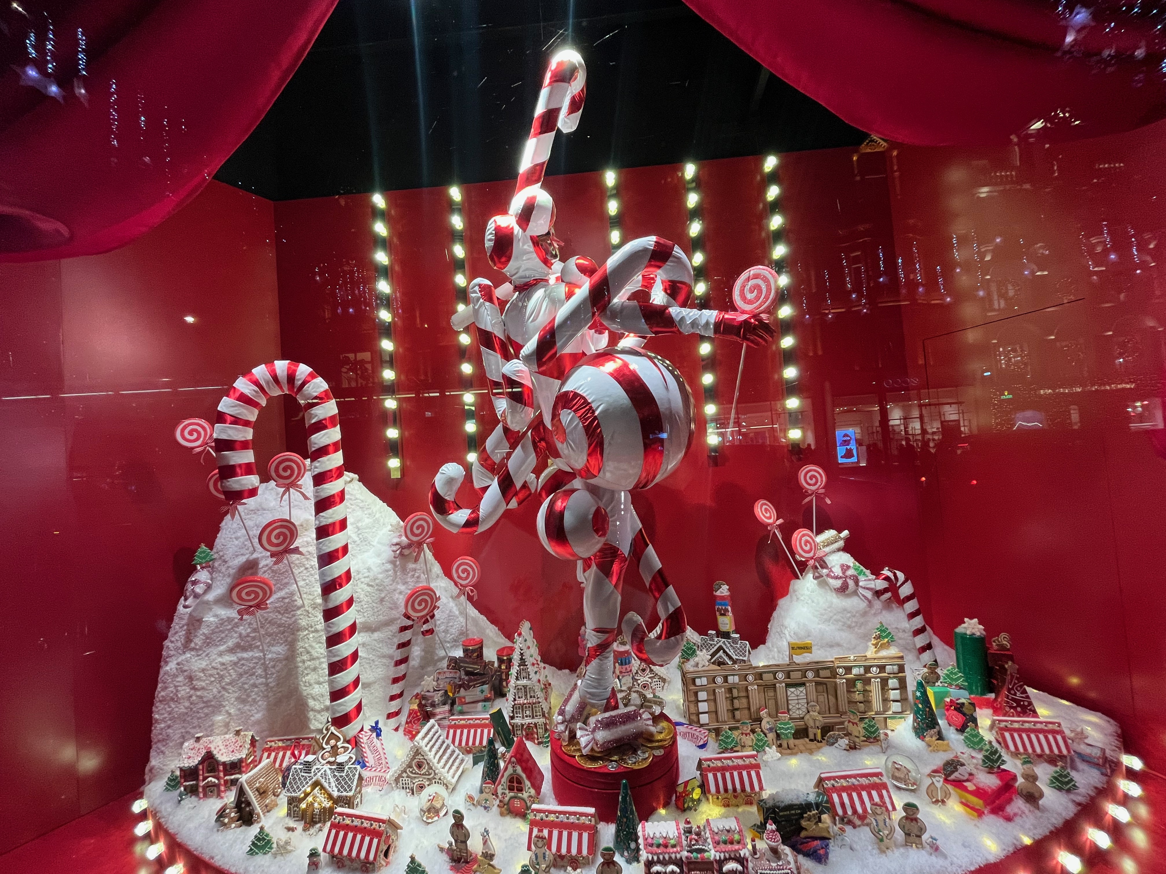 Selfridges window display, showing a tangled collection of large red and white striped candy canes and lollipops. On the floor around them are lots of little models of houses, some with red and white striped roofs, while some other roofs have snow on them. There's also a model of the Selfridges store.