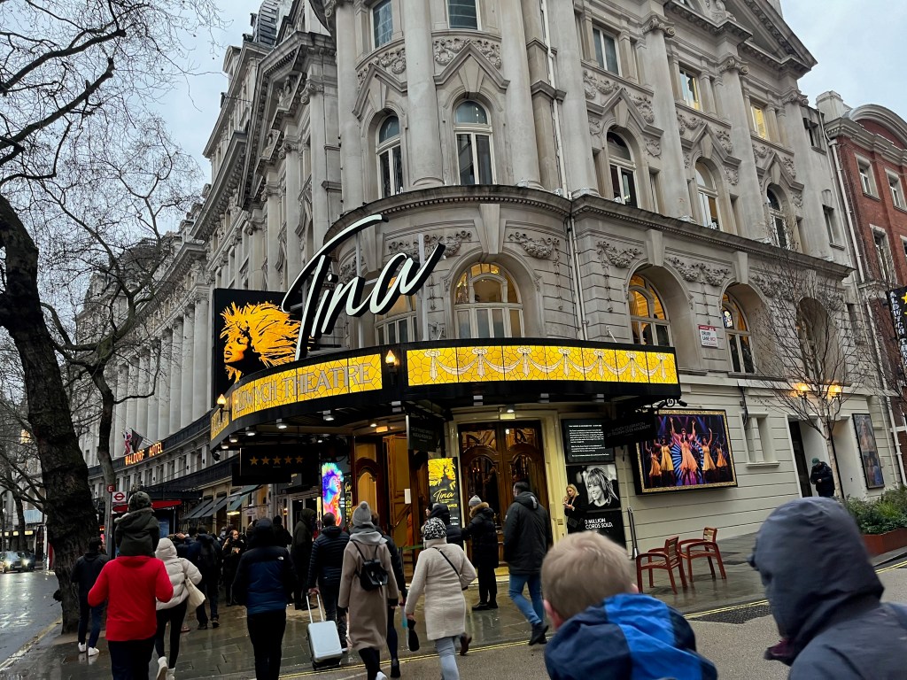The exterior of the Aldwych Theatre, with a signature of the name Tina in white lettering next to a yellow silhouette of Tina Turner against a black background above the entrance.