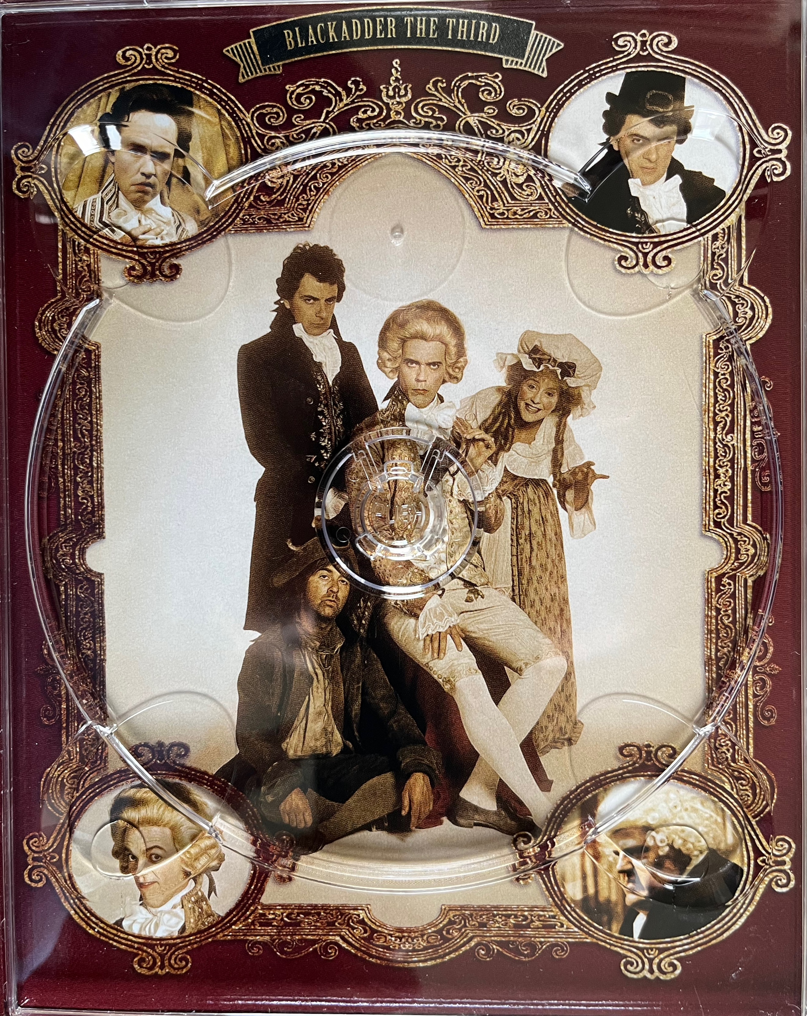 Artwork behind the disc holder for Series 3 of Blackadder in the Complete Collection Blu-ray box set. A large image in the centre shows Blackadder, Baldrick, George and Mrs Miggins posing together, while an ornate gold frame around the edge has circles in each corner with the faces of Lord Smedley, Blackadder, George and Samuel Johnson