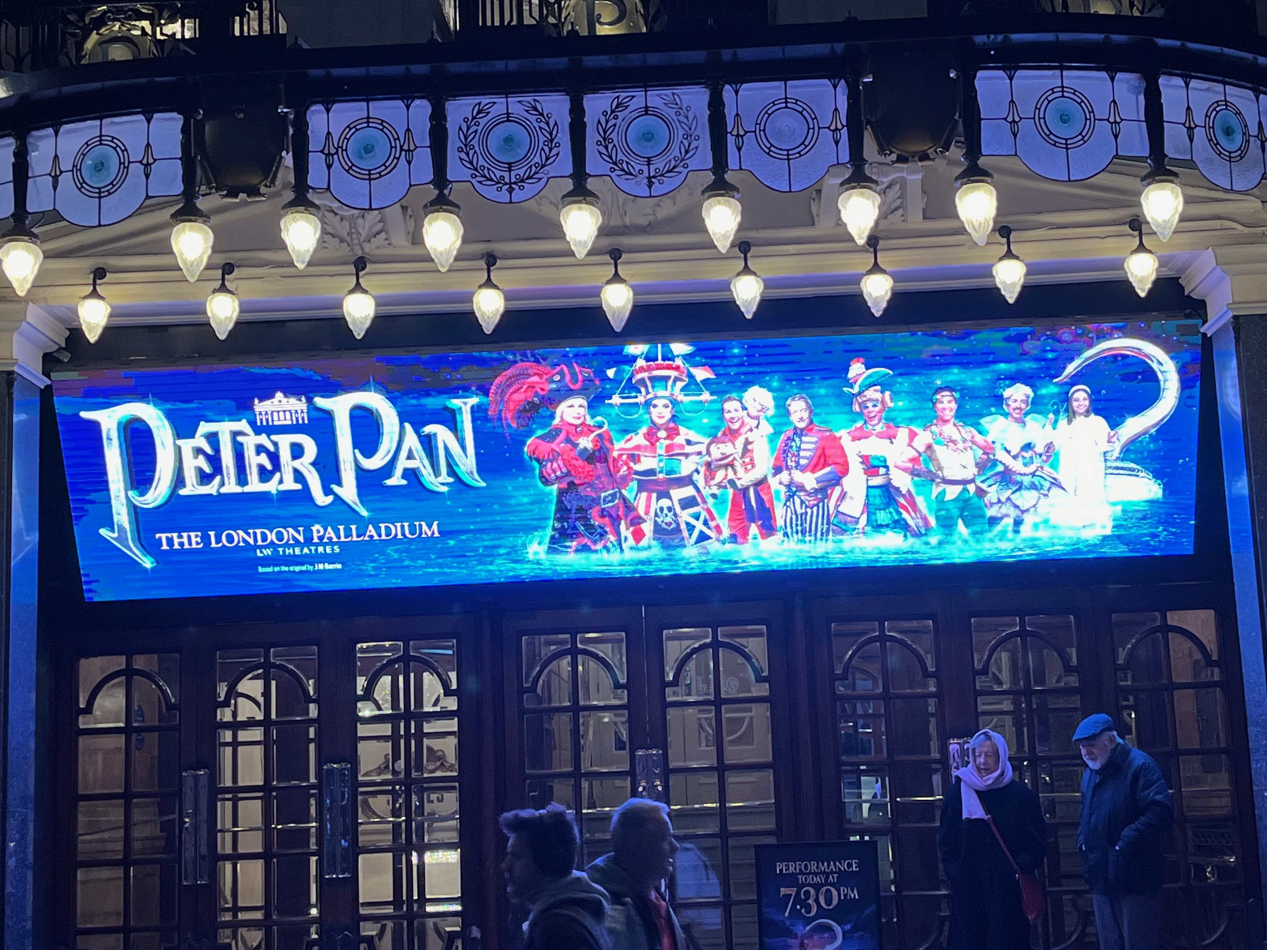 The wide screen above the entrance to the London Palladium, showing the title of the pantomime Peter Pan along with an image of the cast, set against a blue background.