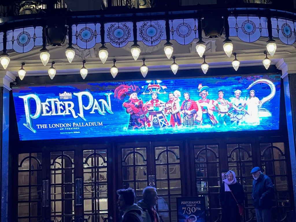 The wide screen above the entrance to the London Palladium, showing the title of the pantomime Peter Pan along with an image of the cast, set against a blue background.