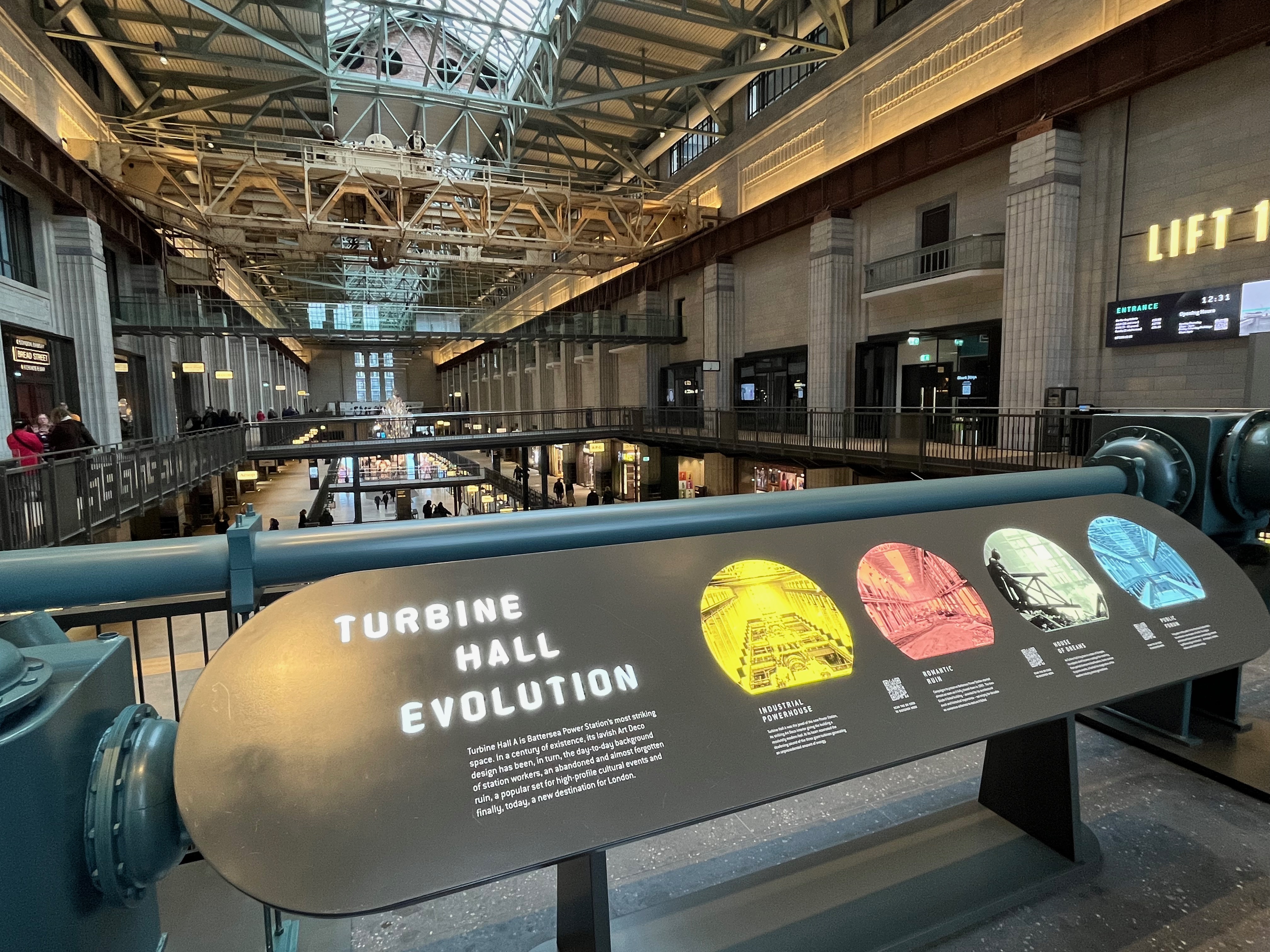 An information panel in the exhibition for Lift 109 in Battersea Power Station, with the heading Turbine Hall Evolution. The length of the actual huge Turbine Hall can be seen stretching into the distance behind it.