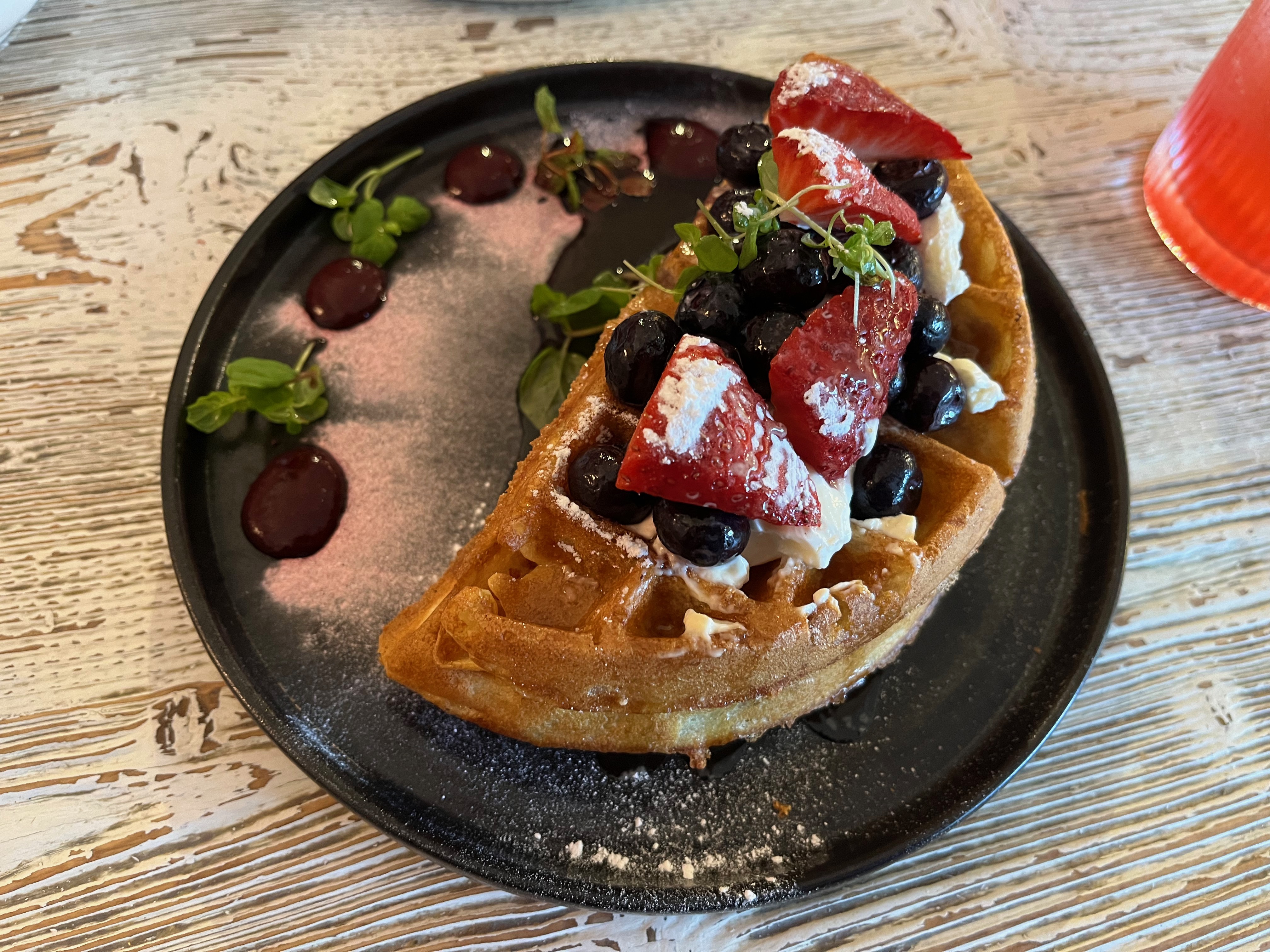 A stack of waffles topped with berries, cream and maple syrup.