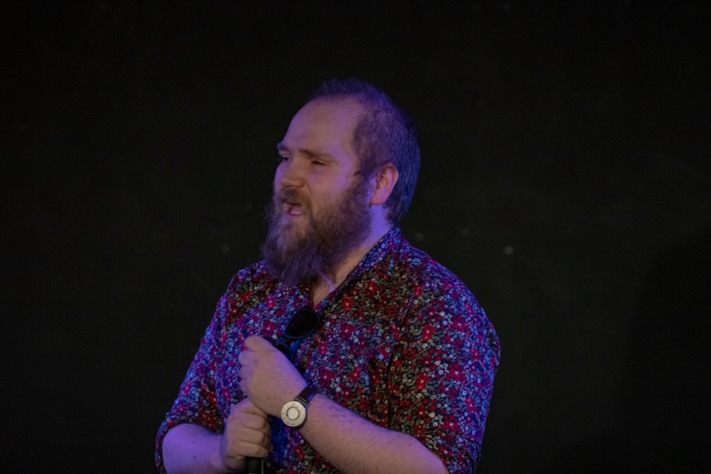 Ben Wilson, a white man with short hair and a blonde beard, wears a floral shirt and talks mid-sentence.