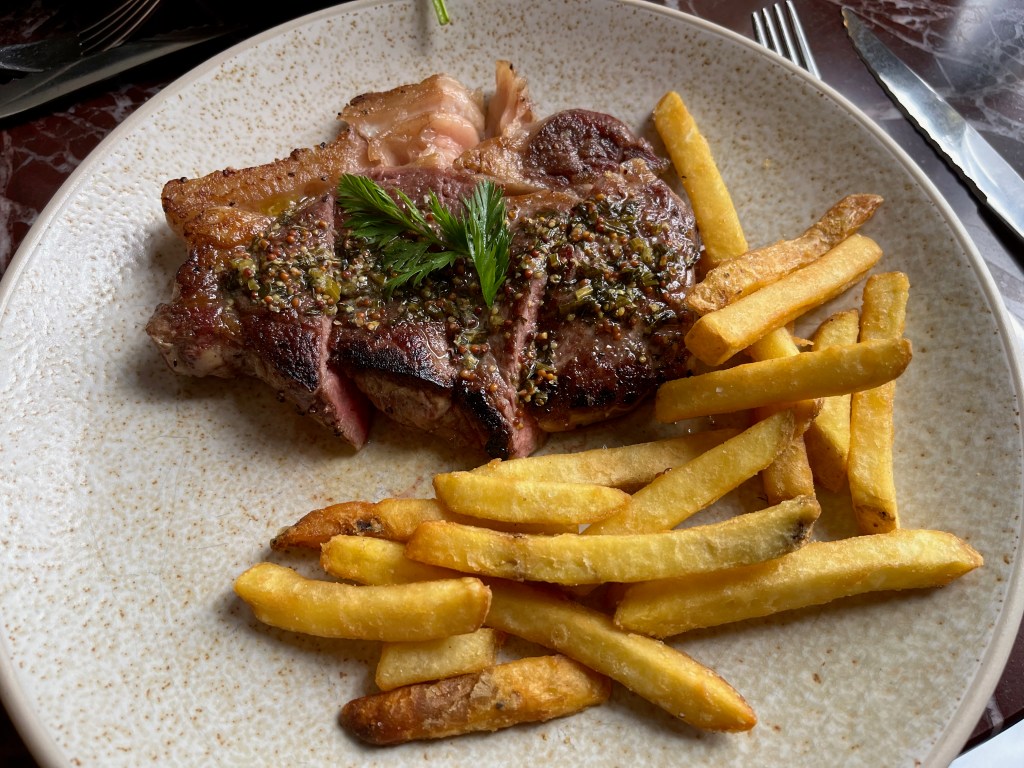 A large, succulent piece of sirloin steak, with a juicy bit of fat on the edge as well, plus some fries.