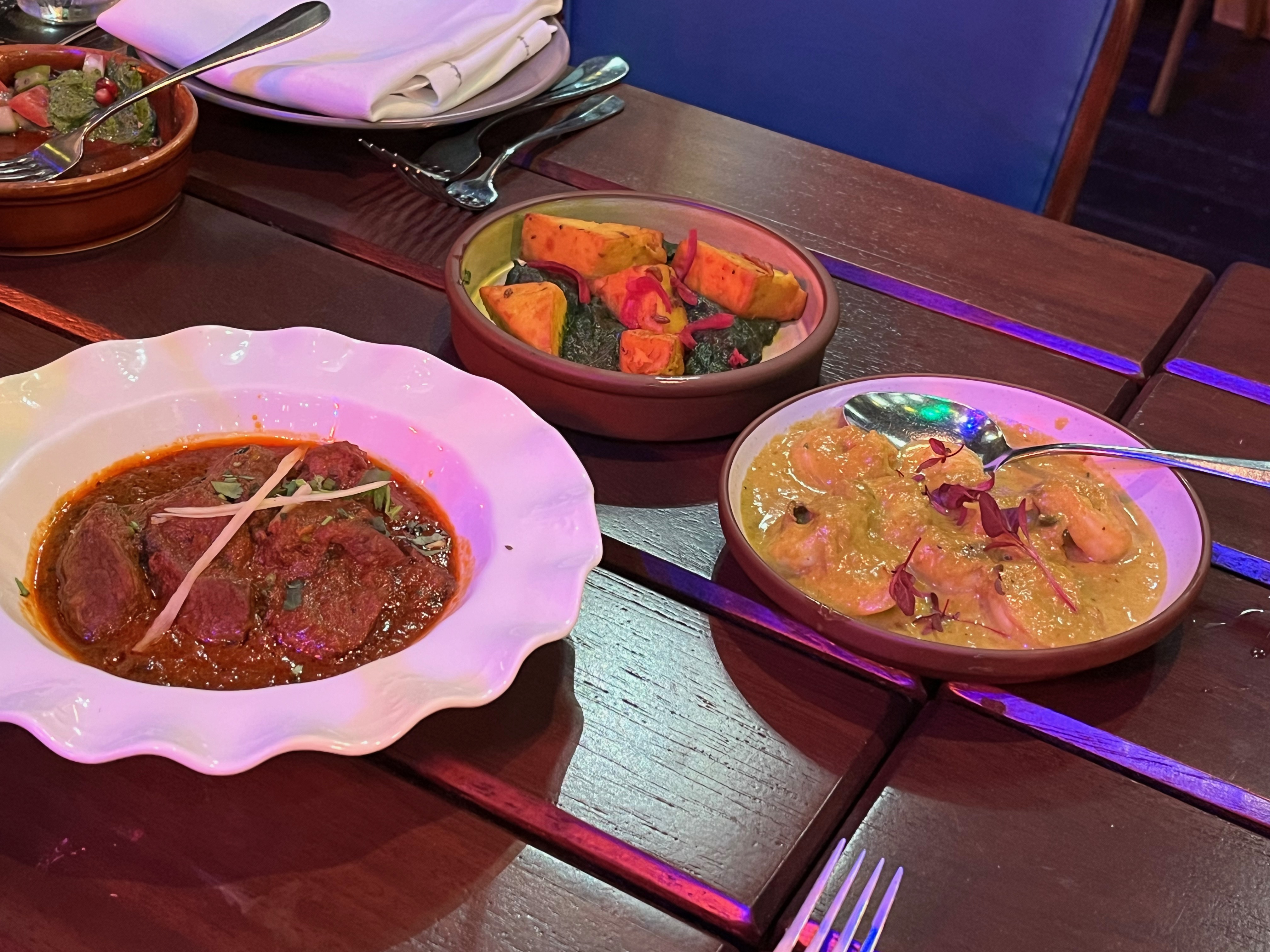 3 plates of food at the Cinnamon Kitchen Holi Feast, including a lamb roganjosh.