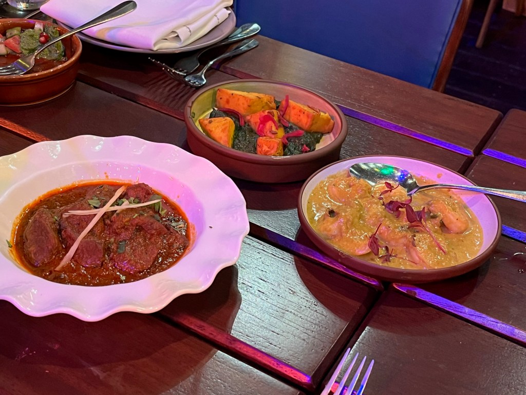 3 plates of food at the Cinnamon Kitchen Holi Feast, including a lamb roganjosh.