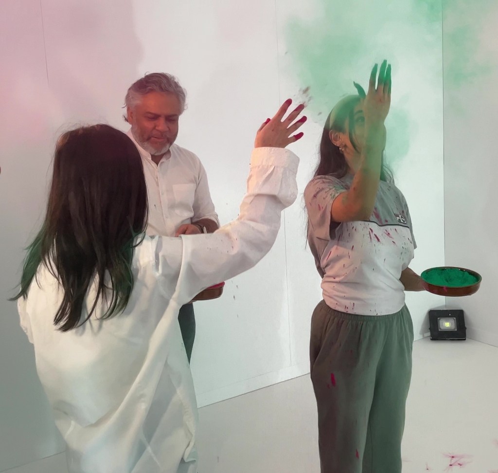 A lady in the white House Of Holi room throwing green powder into the air.