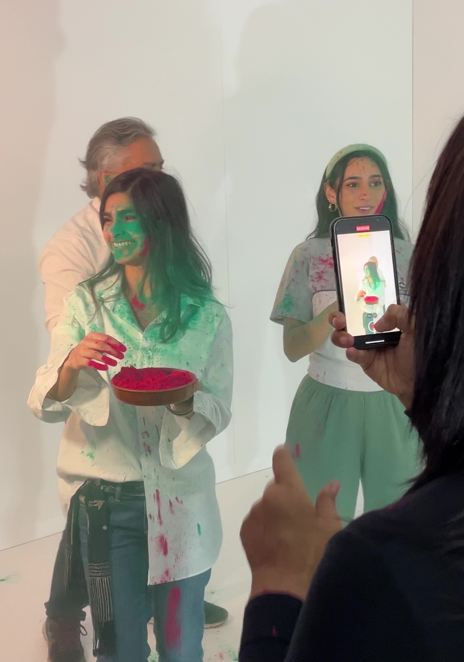 Two ladies smiling in the white House of Holi room, their faces covered in green powder.