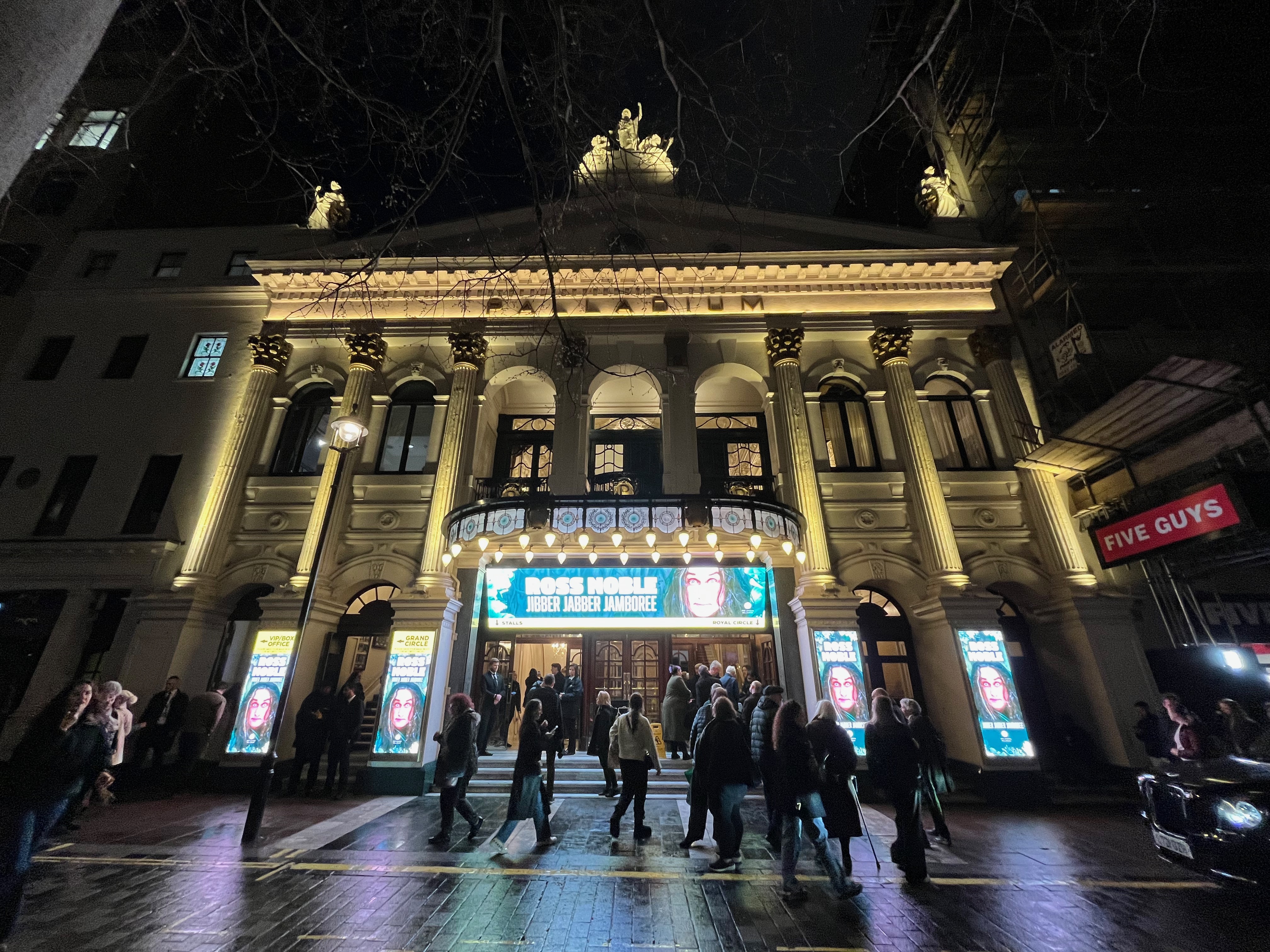 The London Palladium lit up at night, advertising Ross Noble's show Jibber Jabber Jamboree on the ground floor and above the entrance.