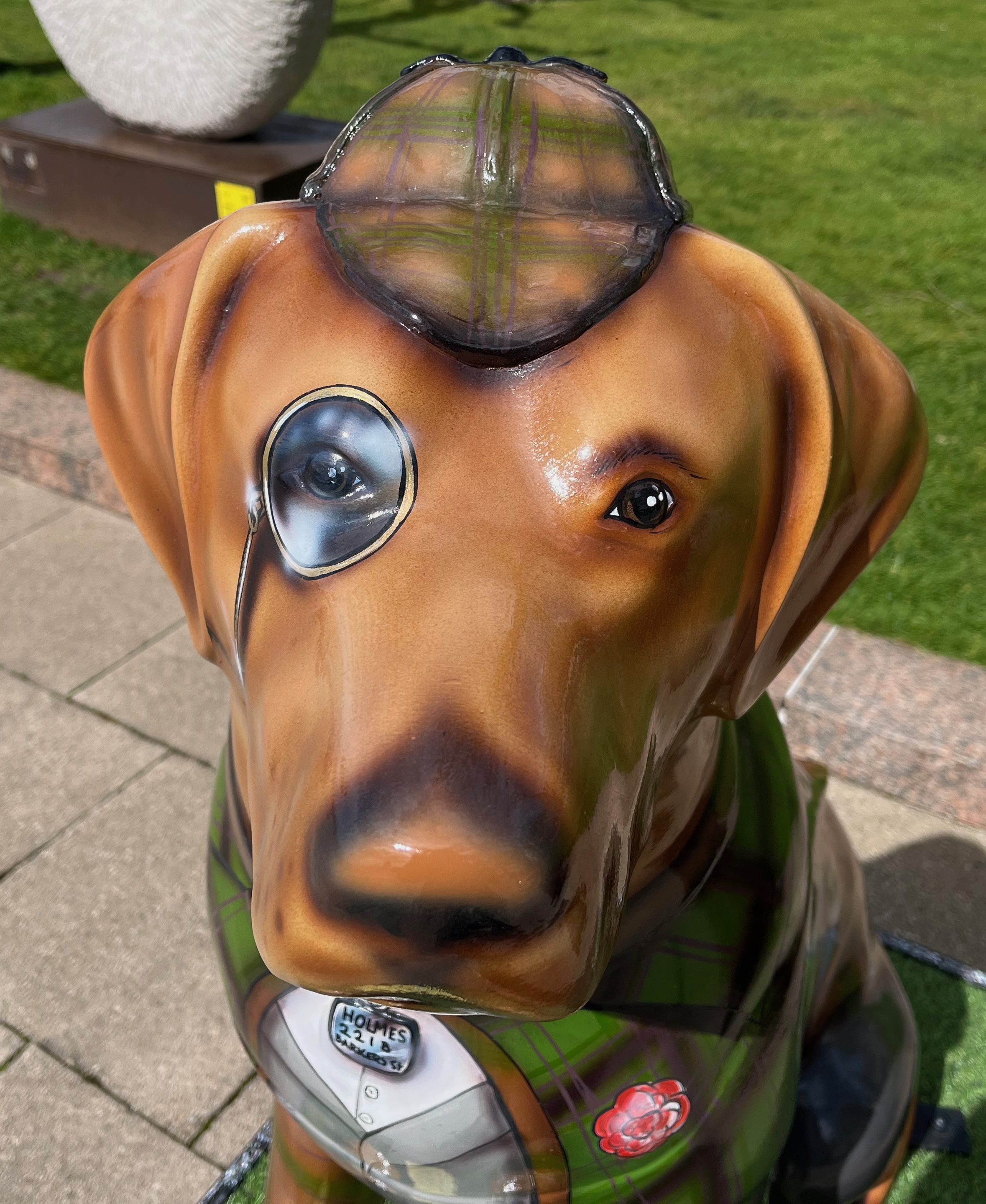 Close-up of the head of a sculpture of a guide dog dressed as Sherlock Holmes, wearing a monocle and a deerstalker hat.