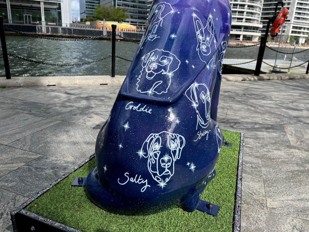 Close-up of the rear of a purple guide dog sculpture, its body covered with stars and constellations in the shapes of dogs' faces. The names of the constellations are written beside them, including Rosy, Meta, Goldie, Stubby and Salty.