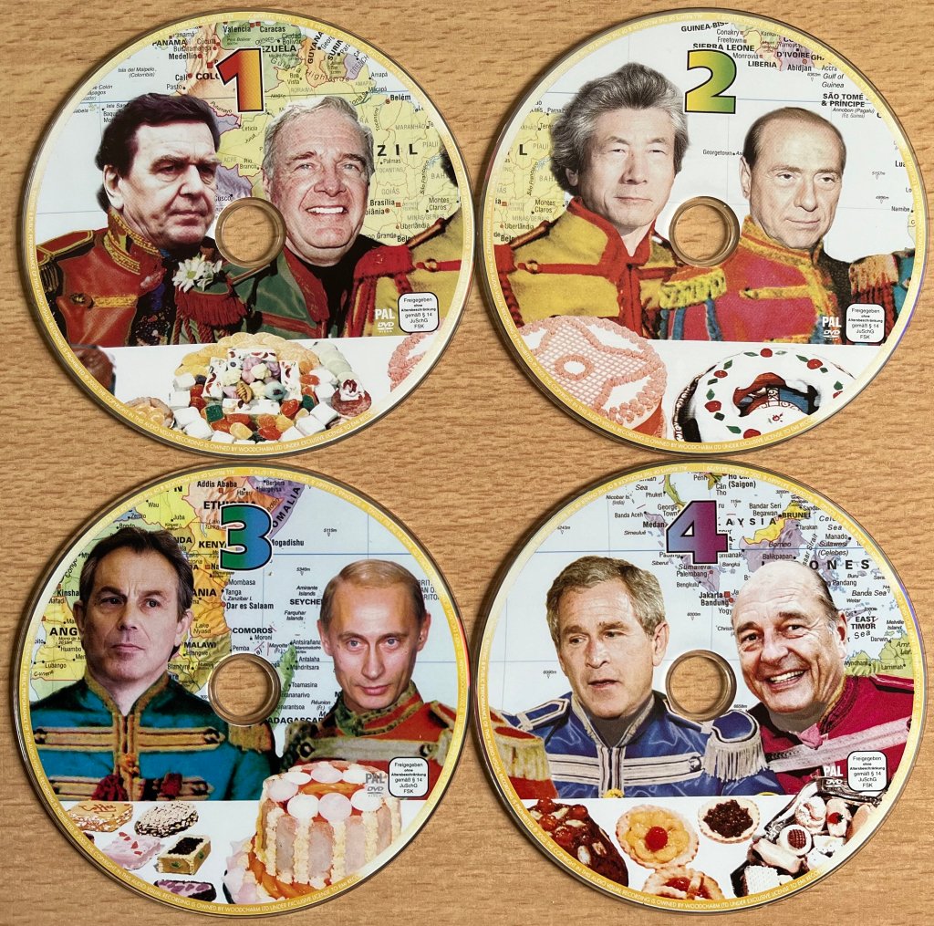 The 4 DVD discs from the Live 8 box set. Each disc shows 2 of the political leaders from the G8 nations, with a colourful map of the world behind them and food on the table in front of them. 
